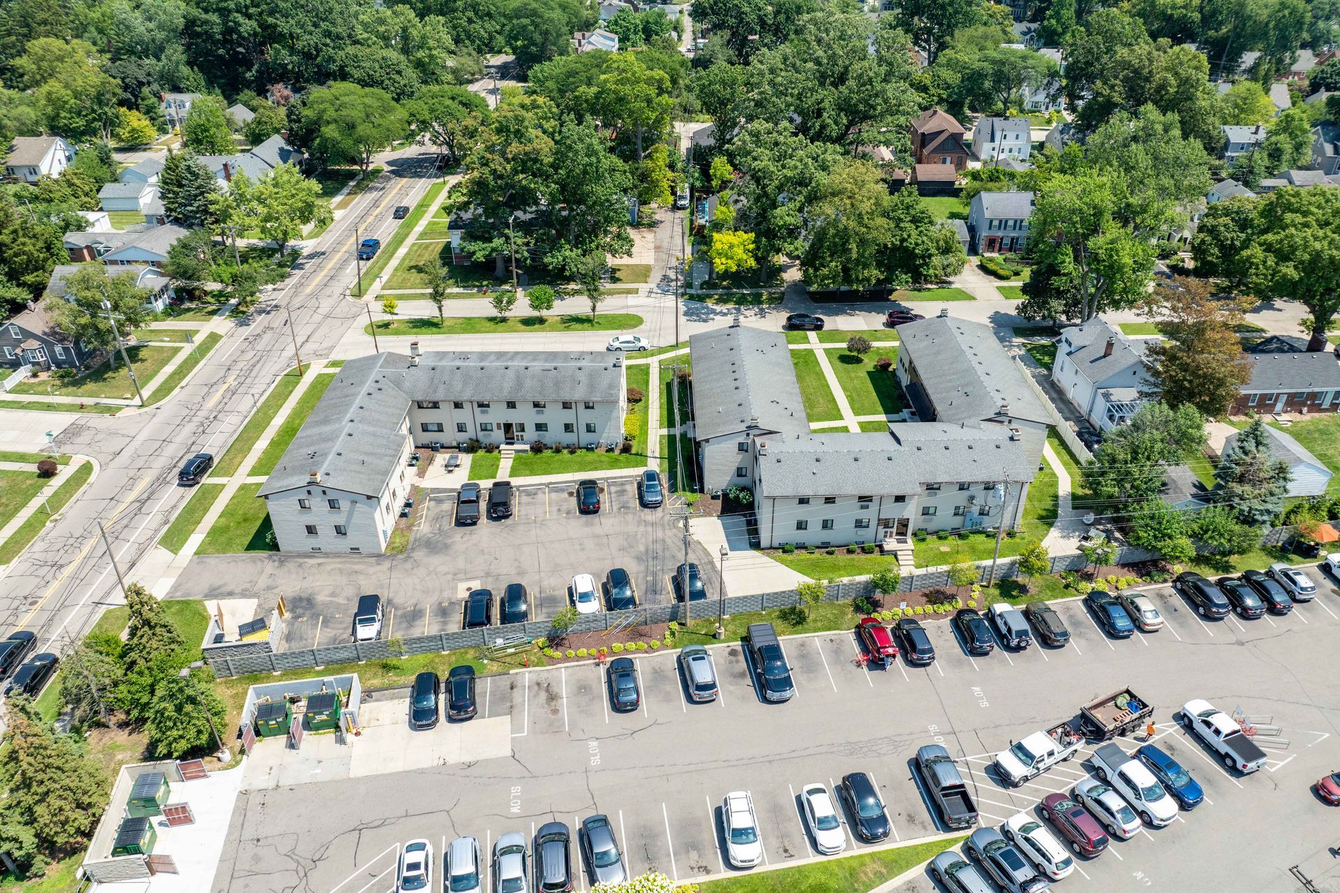 Aerial view of multi-unit housing with parking lot and trees in a residential area.