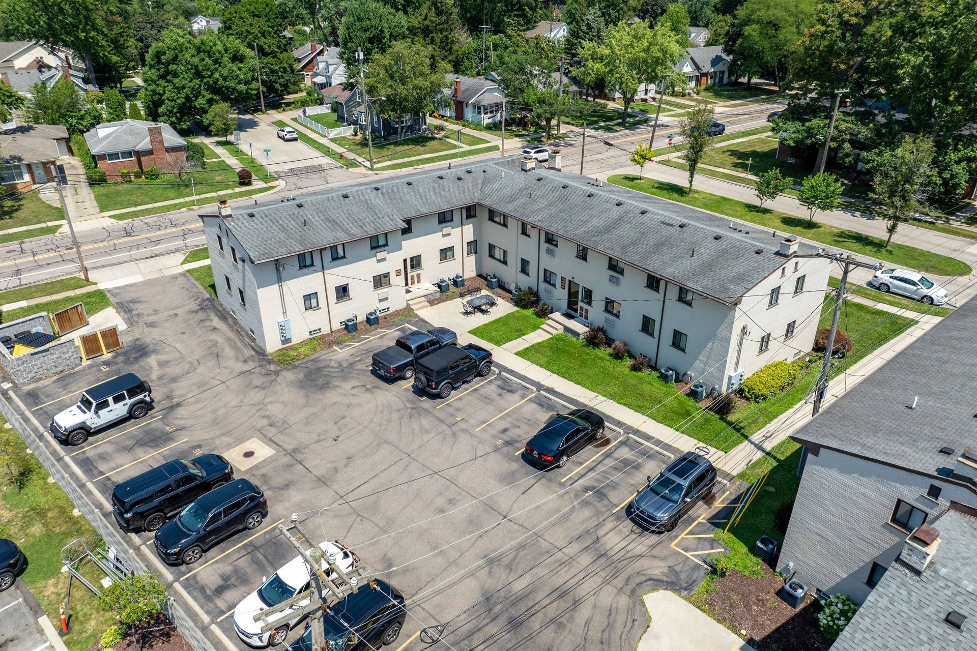 Apartment complex with parking lot; white building with gray roof, cars parked, sunny day.