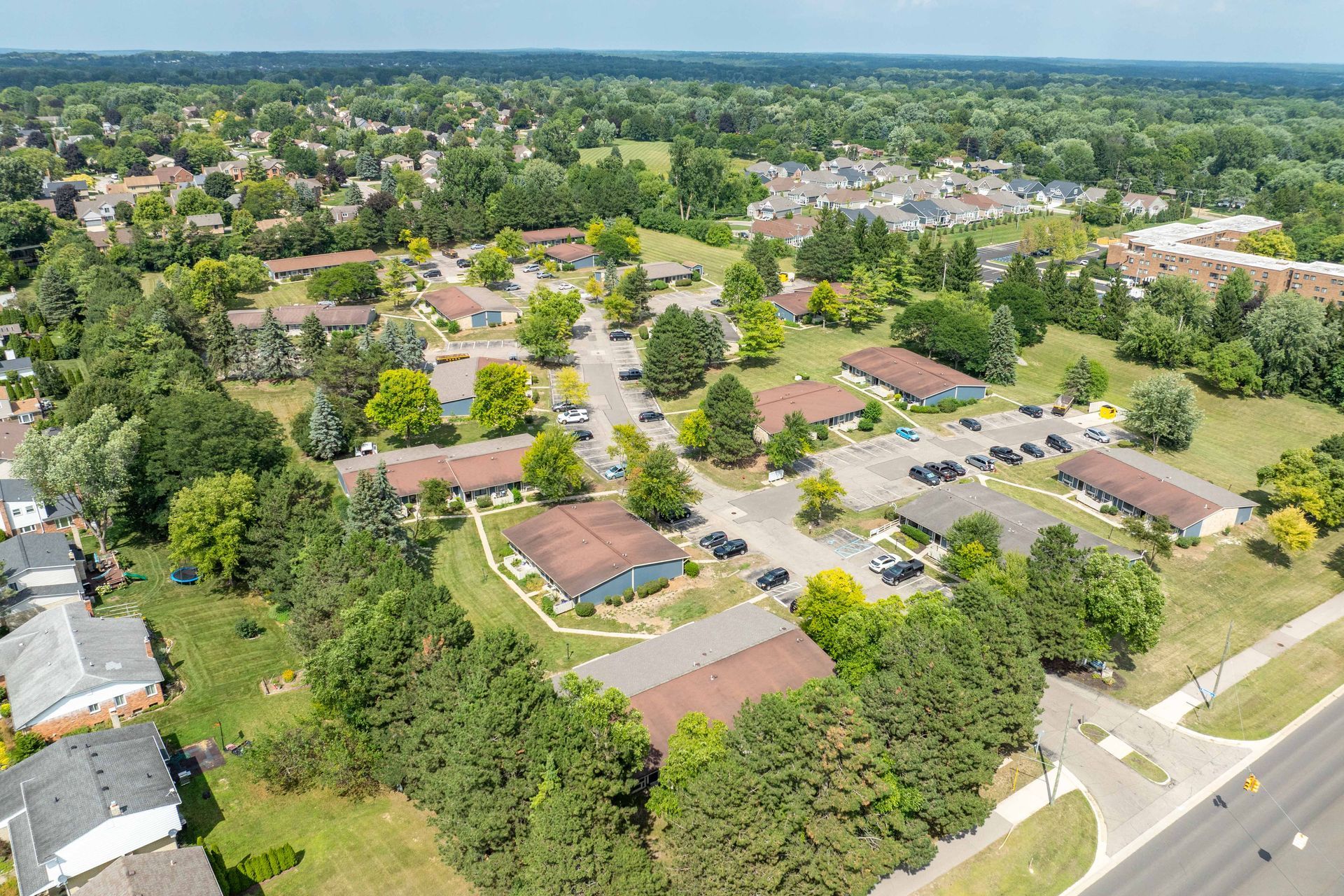 Aerial view of a suburban neighborhood with houses, trees, and a parking lot on a sunny day.