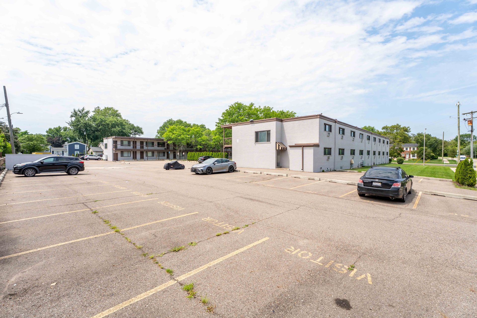A parking lot with cars in front of a two-story, gray motel building on a sunny day.