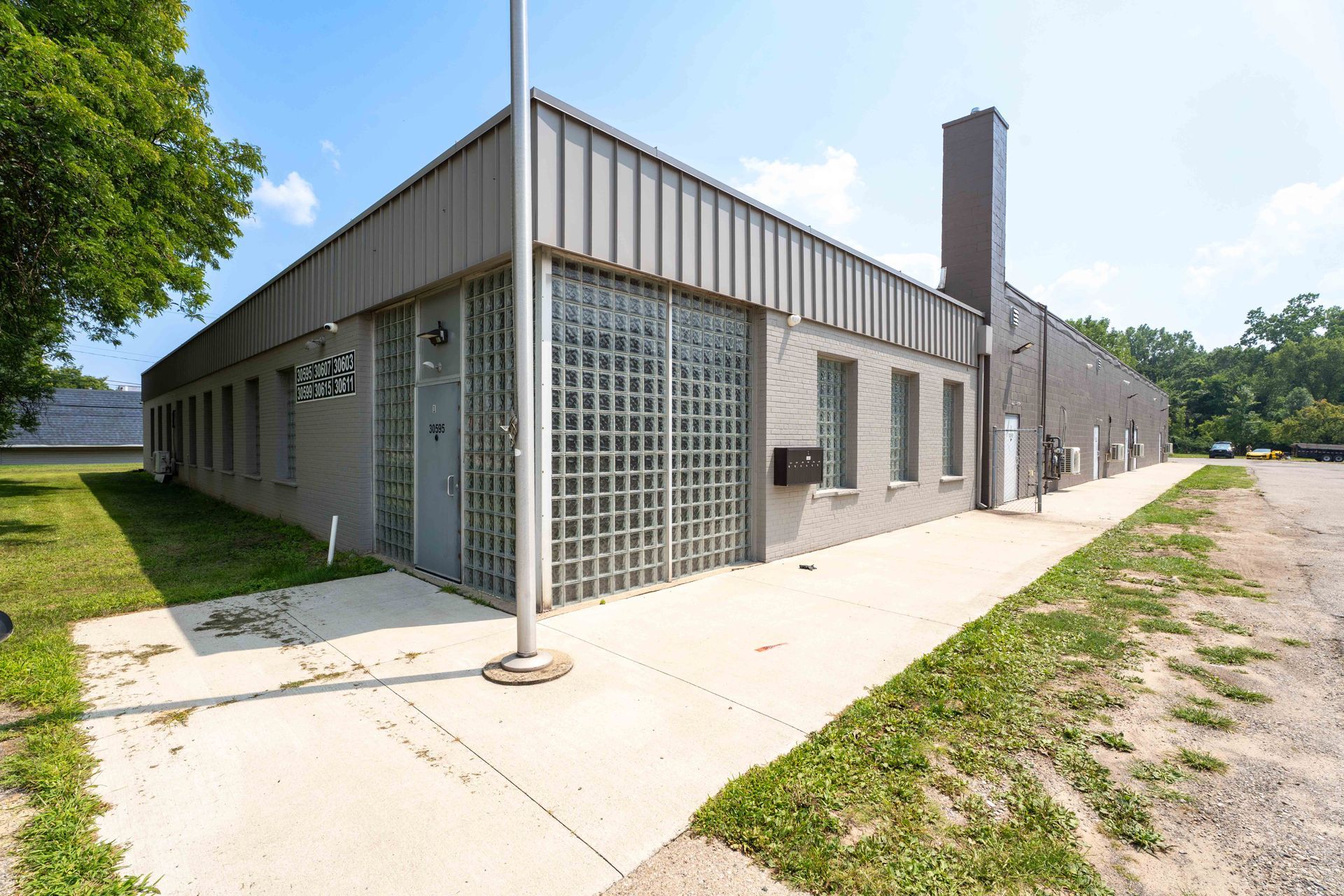Gray industrial building with glass block windows and a sidewalk on a sunny day.