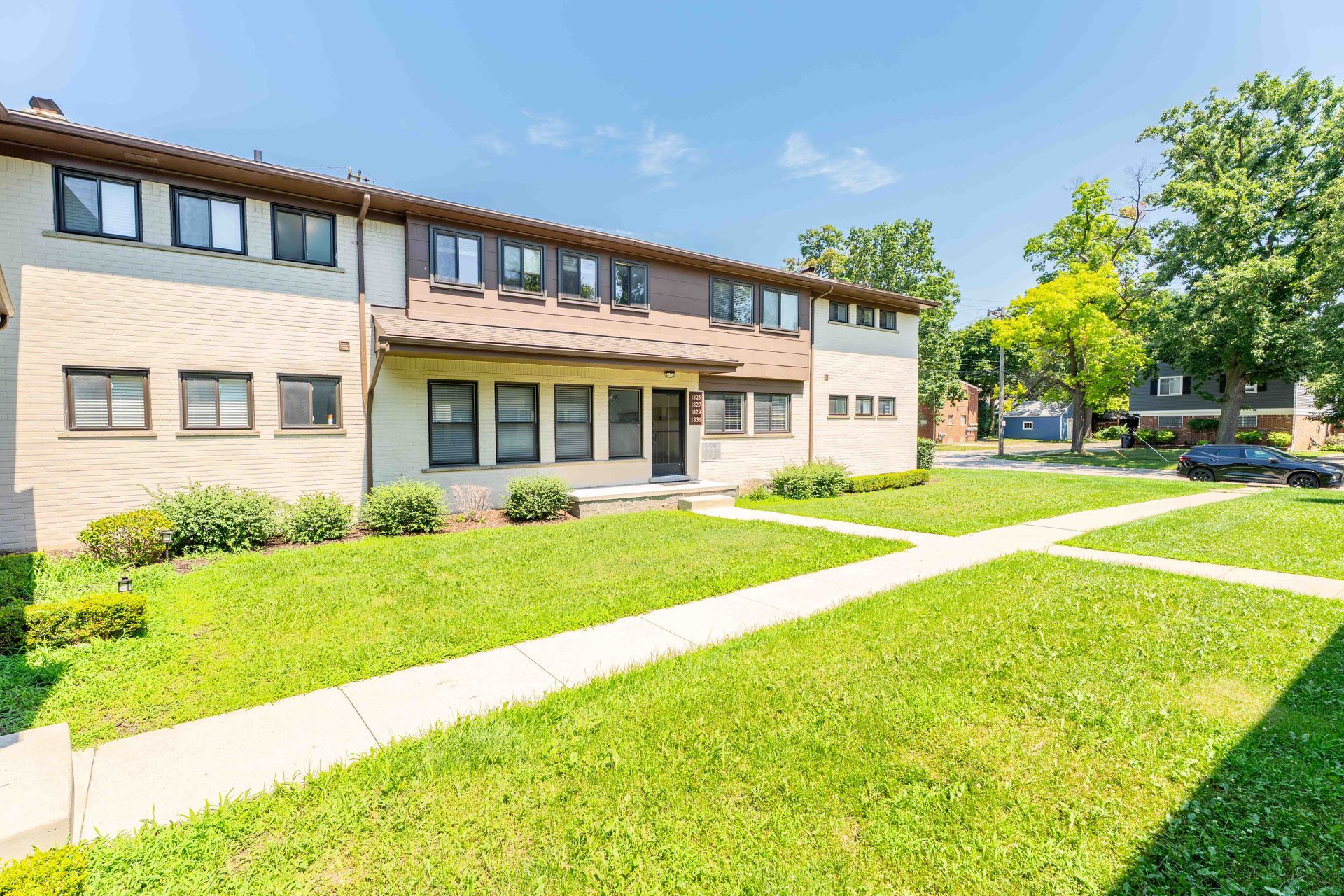 Two-story townhouses with brown trim and a pathway in a grassy area under a blue sky.