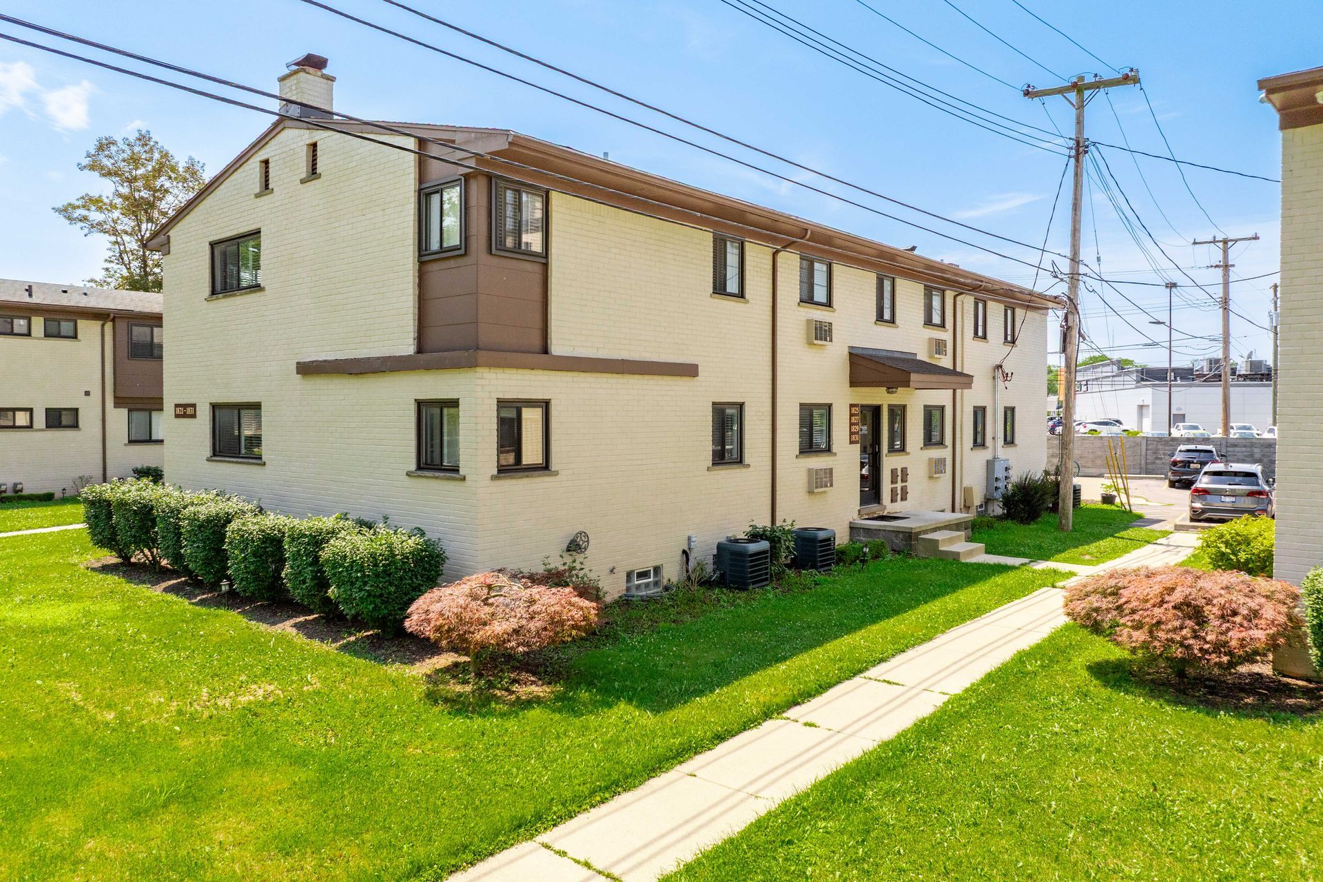 Two-story beige apartment building with brown trim and green lawn on a sunny day.