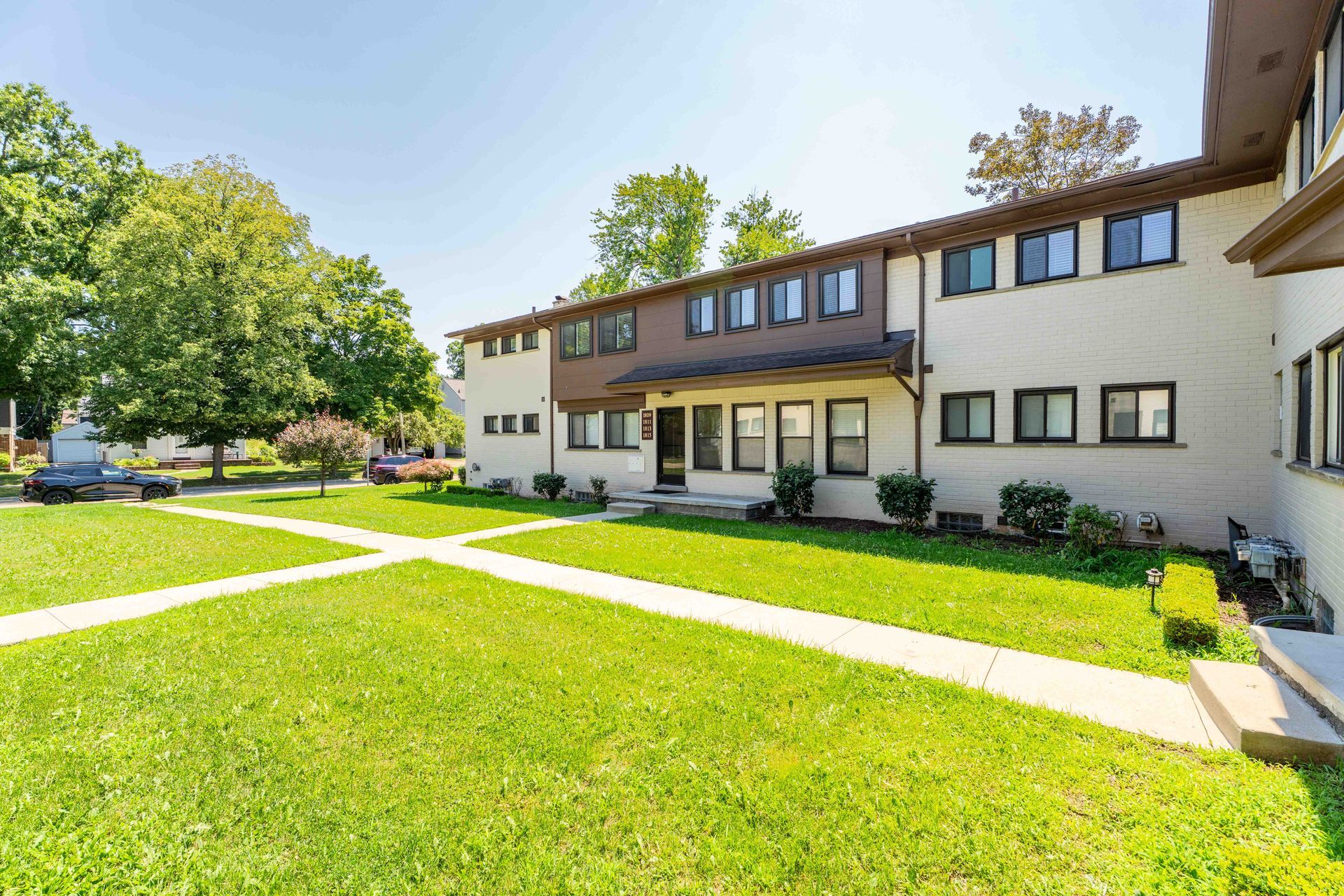 Row of tan and brown townhomes with green lawn and walkway on a sunny day.