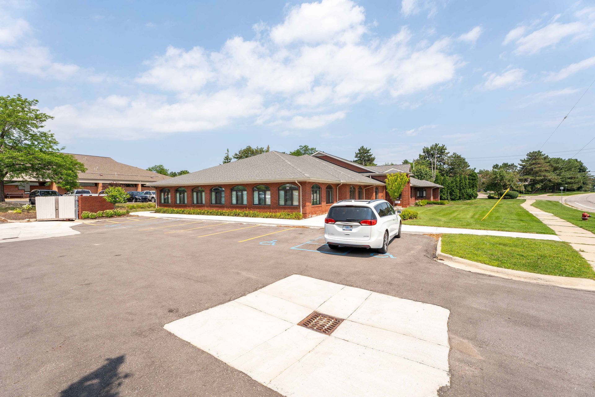 Exterior of a one-story brick building on a sunny day; white van parked in front.