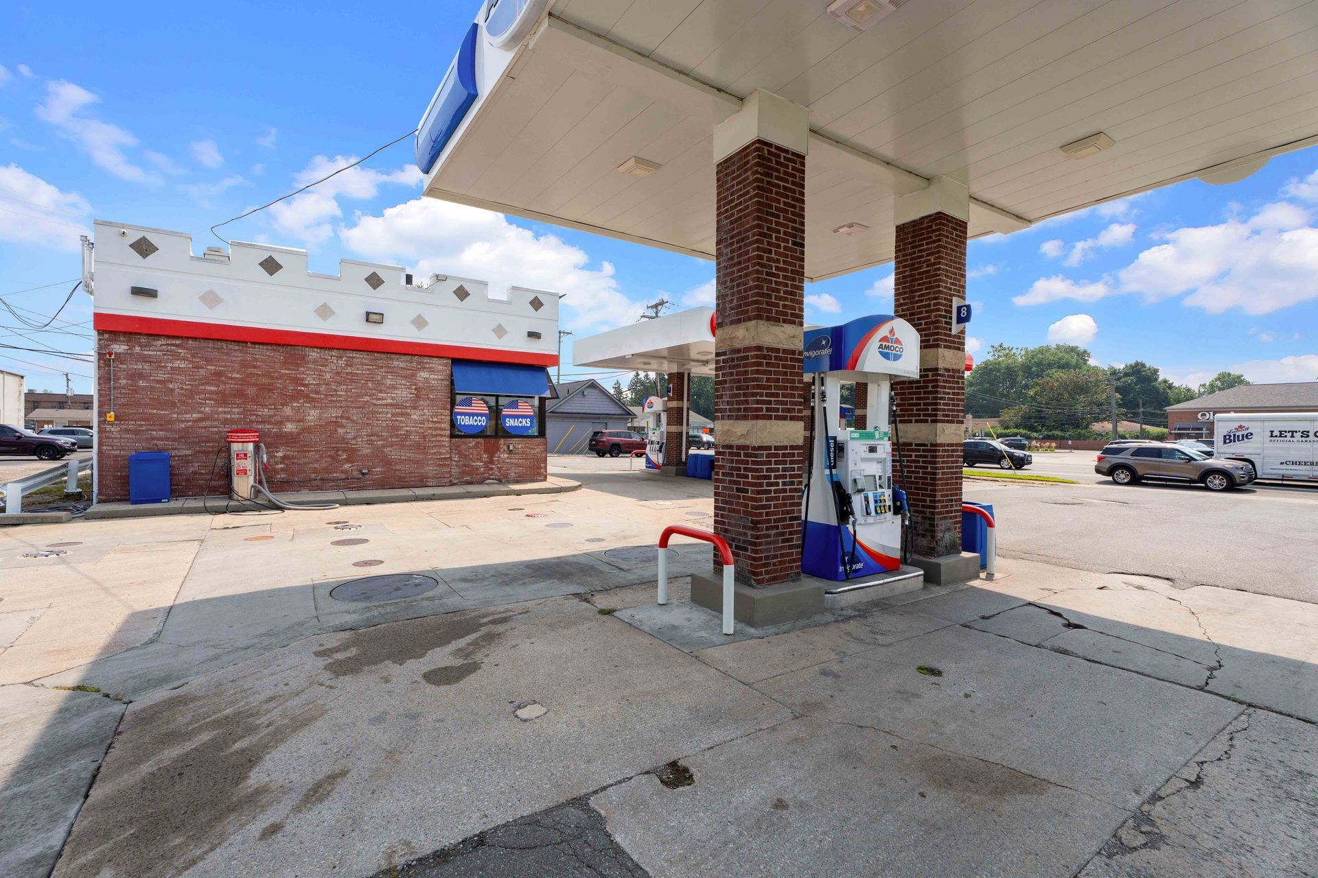 Gas station with red brick building and canopy, gas pumps, blue sky.