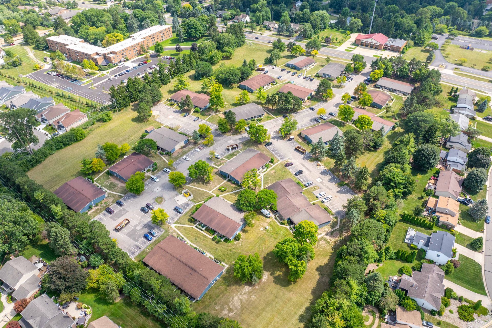 Aerial view of a residential community with brown-roofed buildings surrounded by green trees and grassy areas.