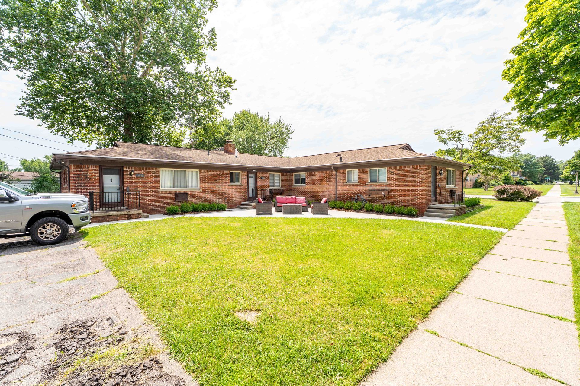 Low-rise brick building with green lawn, sidewalk, parked truck, and seating area.