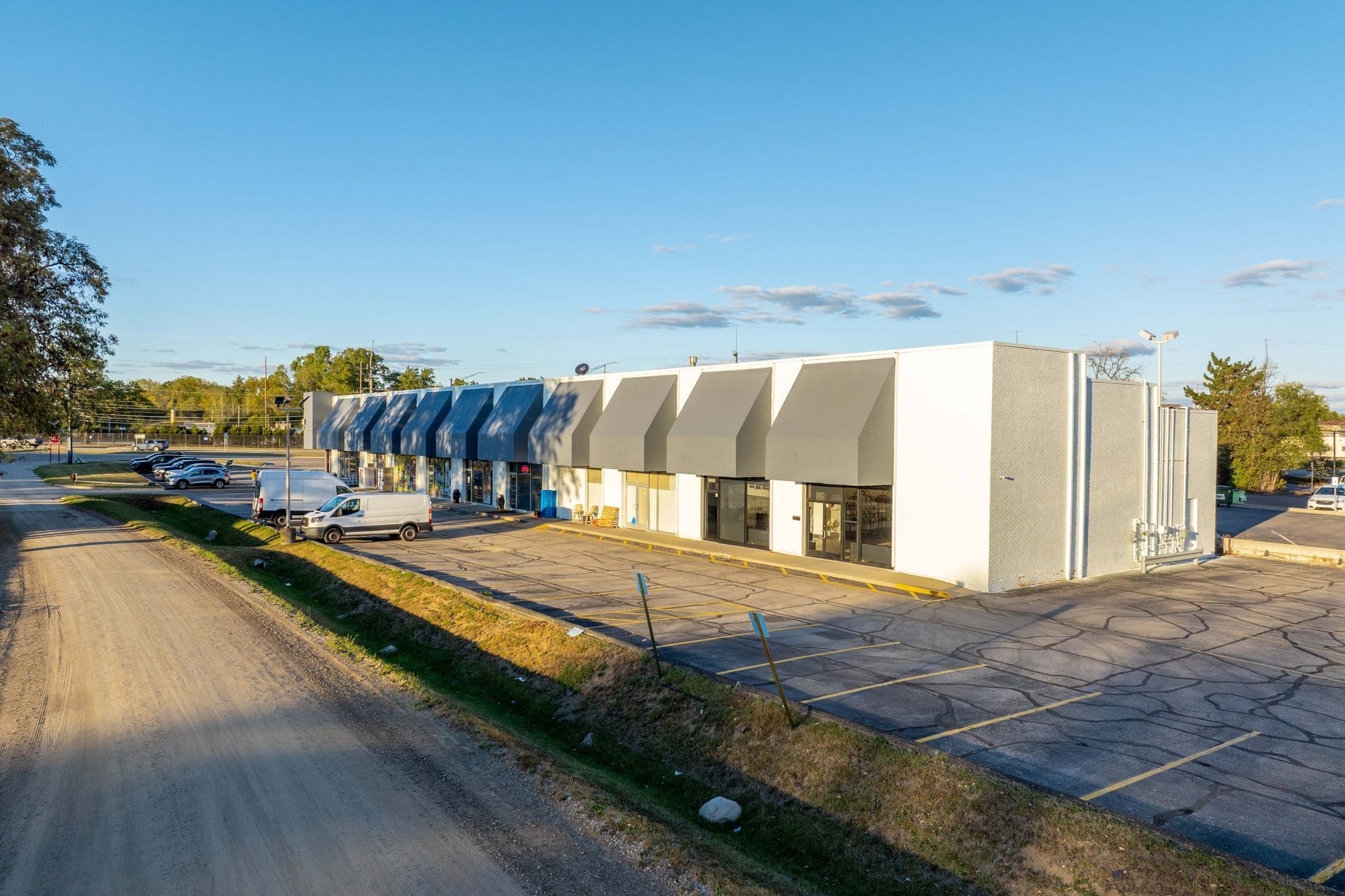 A commercial building with gray and white facade, awnings, and a parking lot.