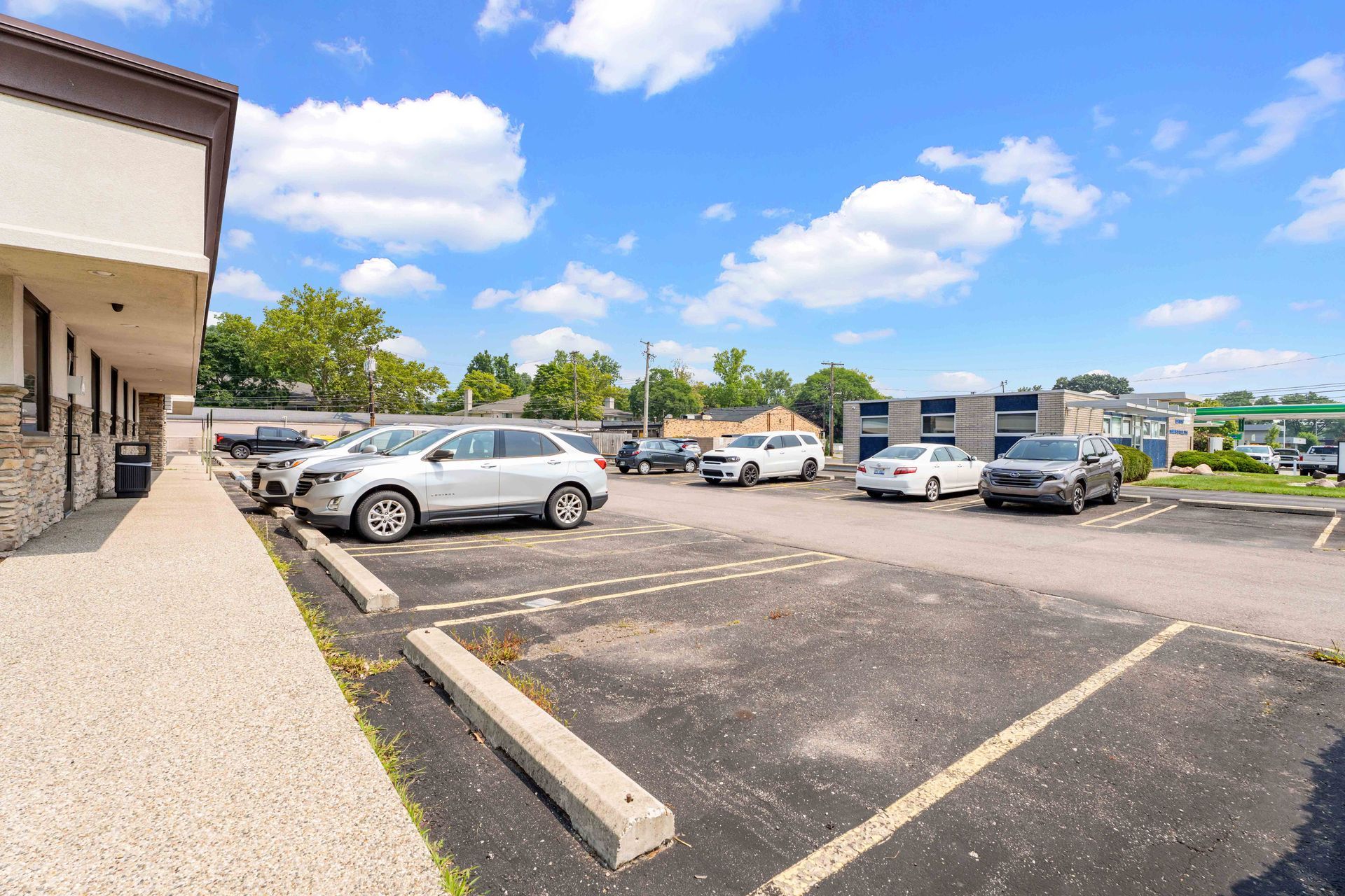 Parking lot with cars parked. Building on left, blue sky with clouds.