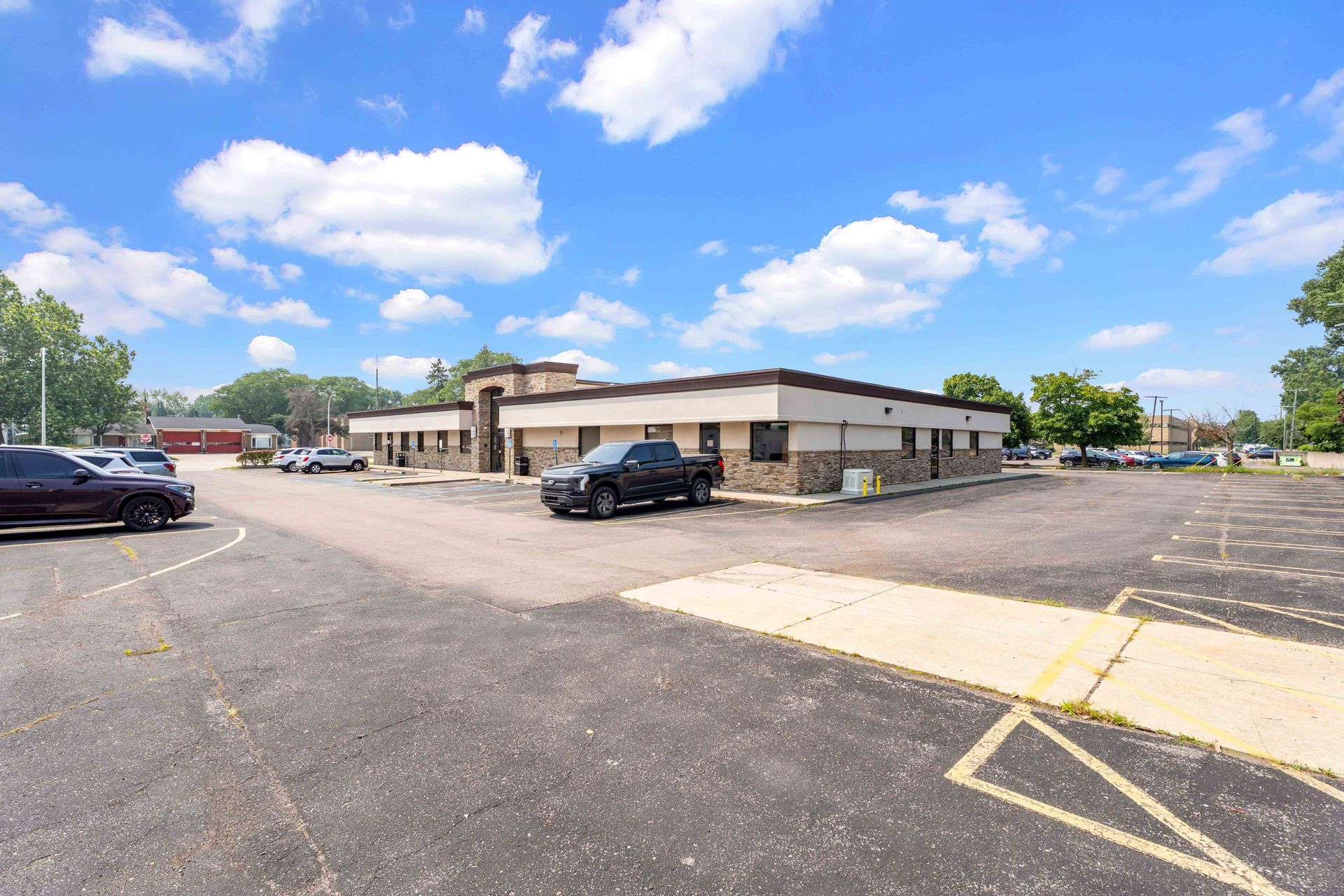 Commercial building with cars parked in front, blue sky with clouds above.