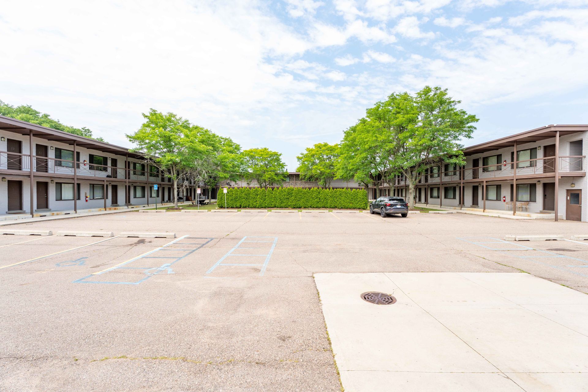 A motel with two symmetrical buildings and a large parking lot, under a partly cloudy sky.