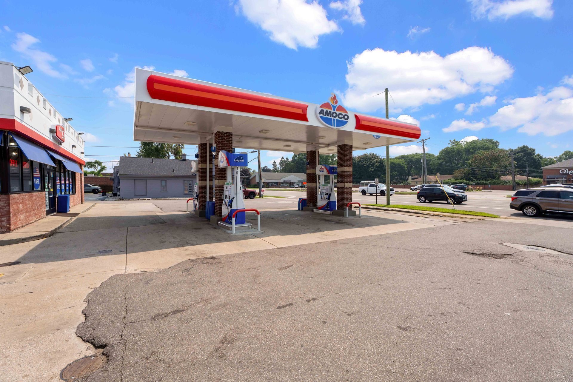 Gas station with red and white canopy, blue signs, and brick building on a sunny day.
