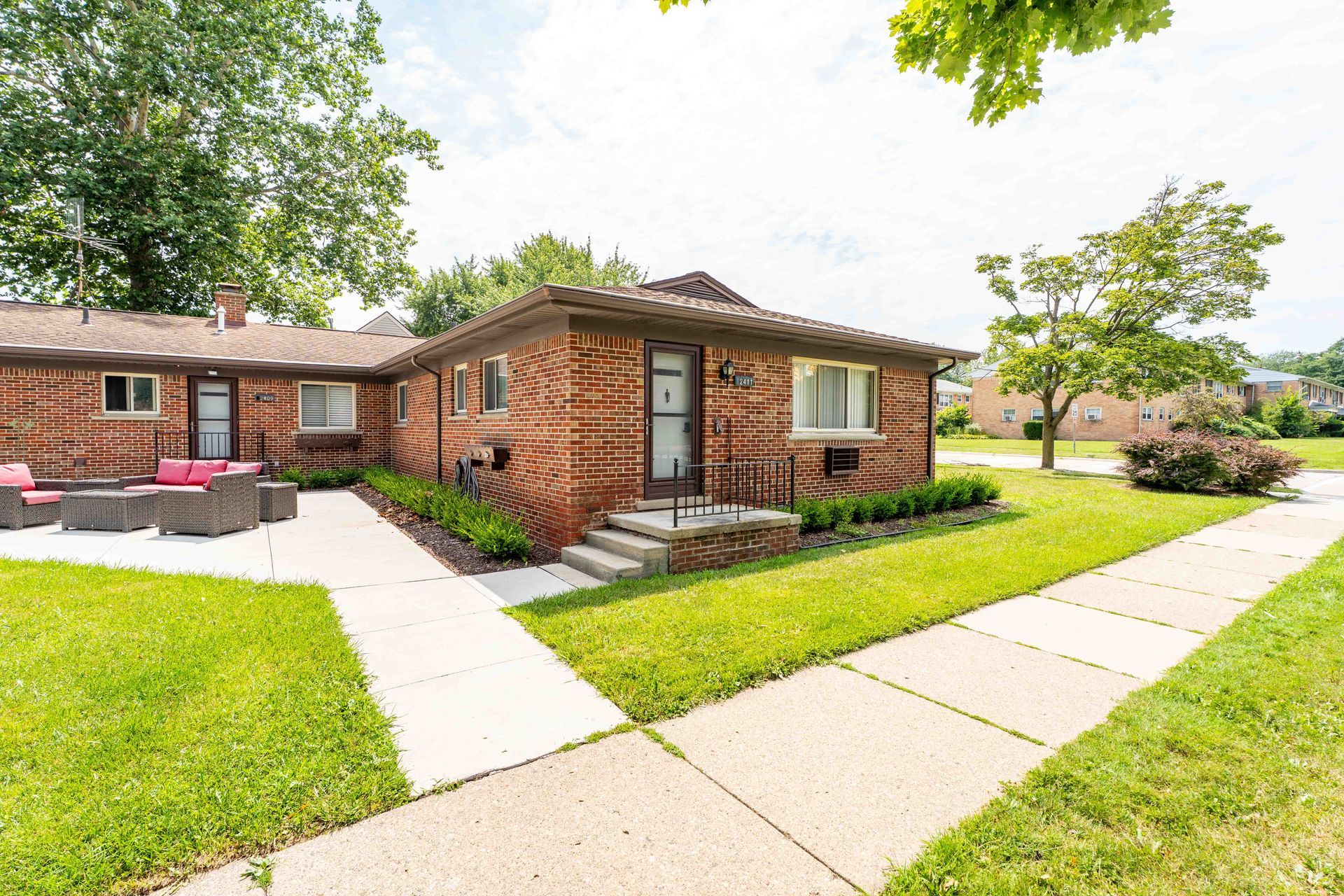 Brick house with green lawn, sidewalk. Pink seating area on the left.