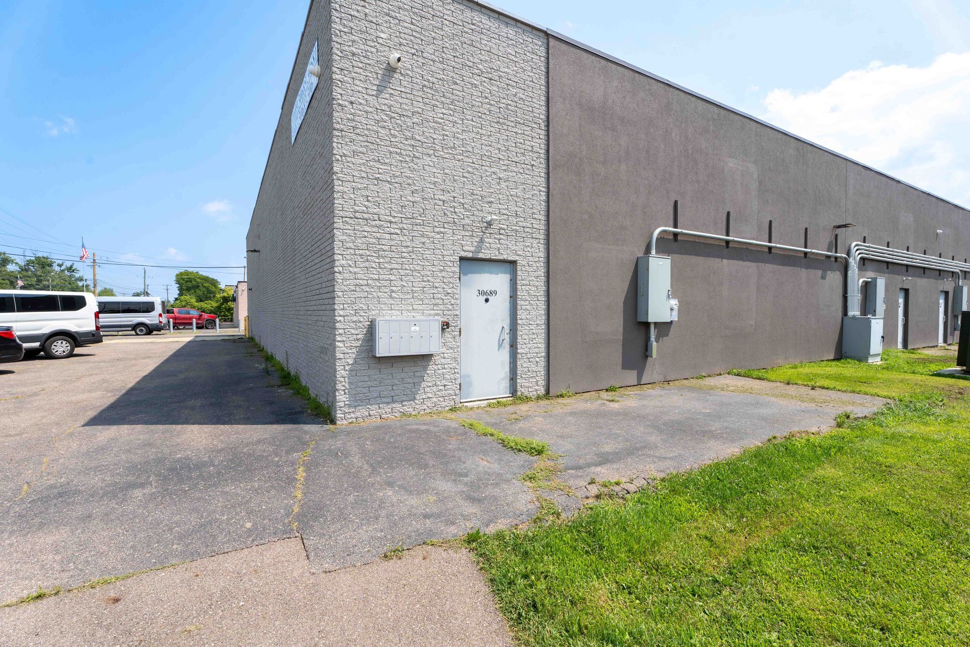 Exterior of a gray commercial building with a concrete walkway, door, and grassy area. Blue sky in background.