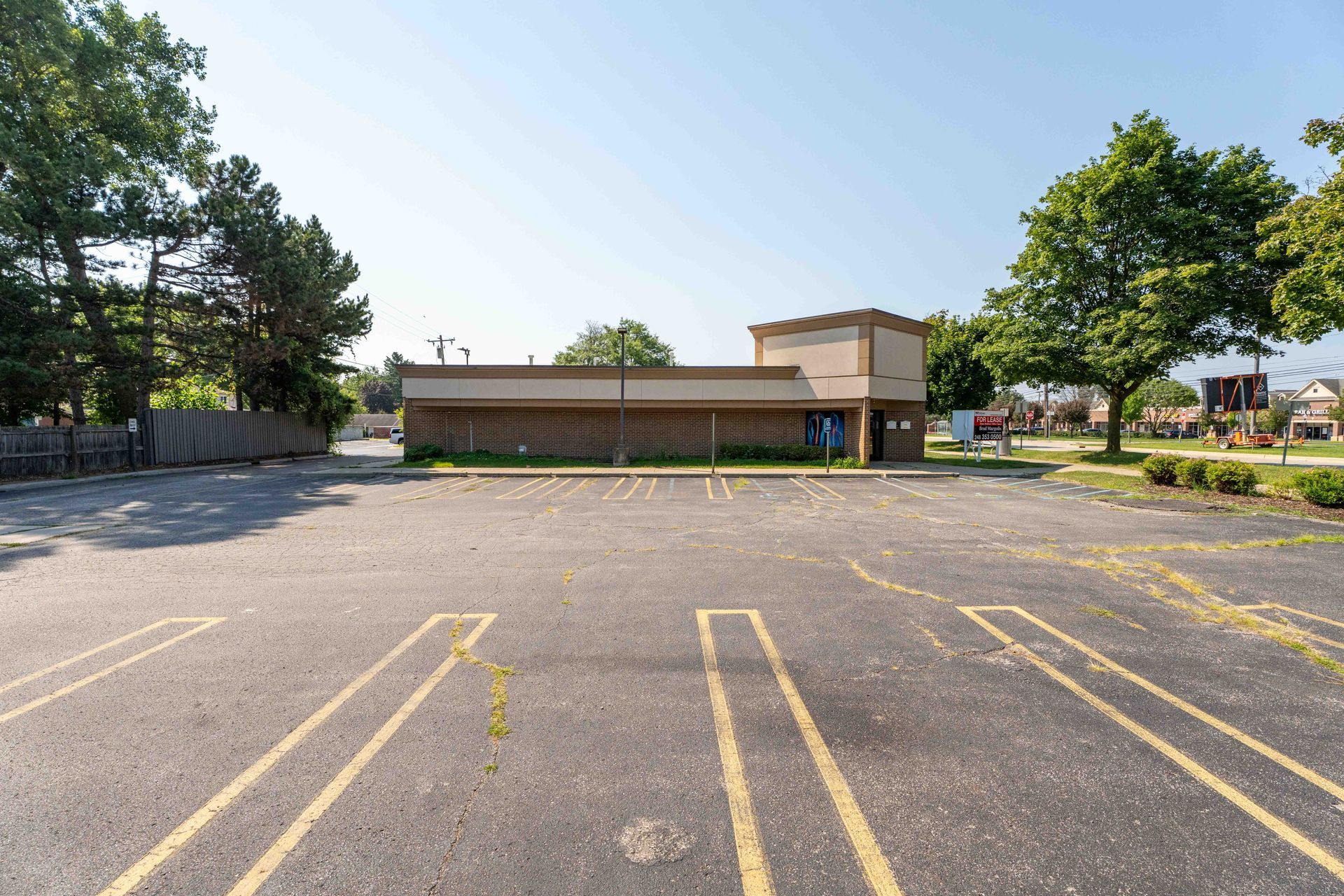 Empty asphalt parking lot in front of a single-story building with trees on either side under a clear sky.