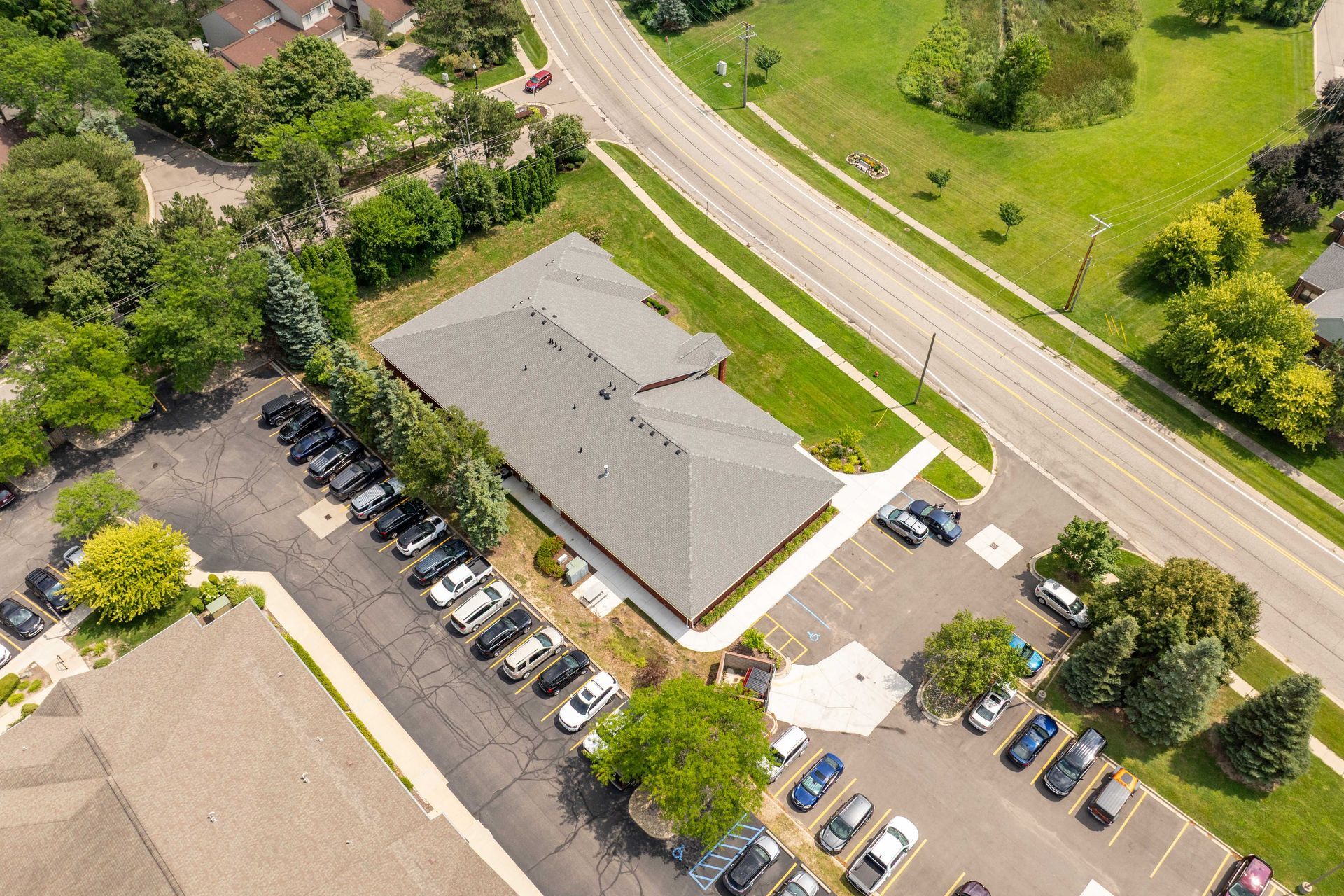 Aerial view of a building with cars in the parking lot. Trees and a road are also visible.