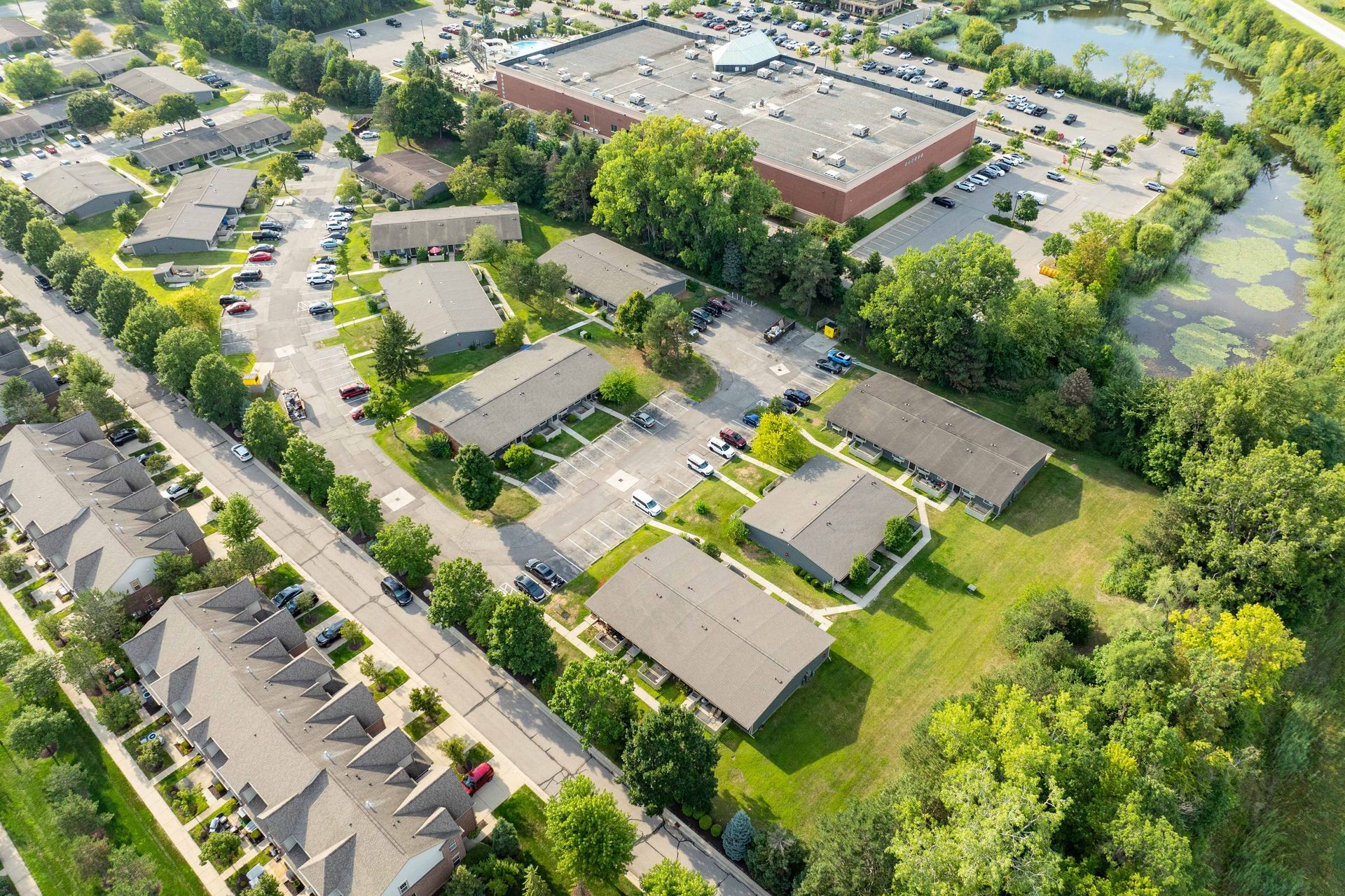 Aerial view of residential buildings, a retail store, and a pond surrounded by trees and greenery.