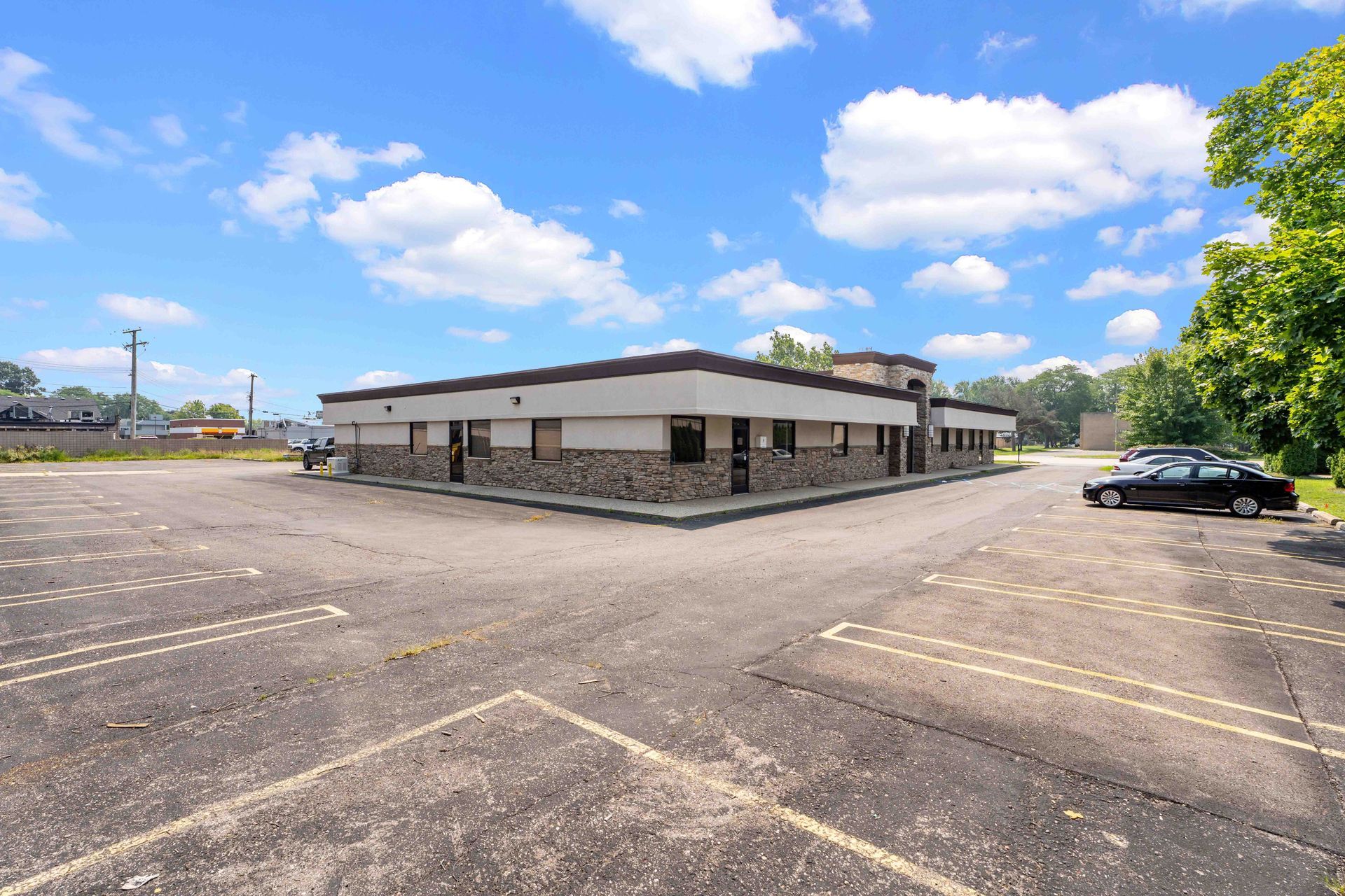 A one-story commercial building with a black car parked in a cracked parking lot on a sunny day.