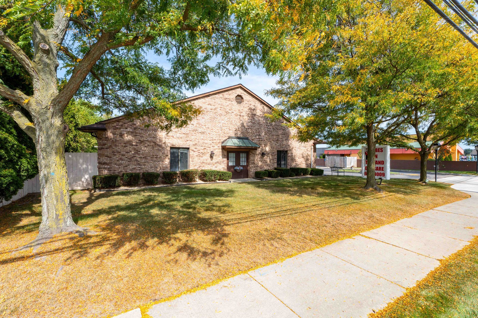 Brick building with trees, a sidewalk, and a lawn.