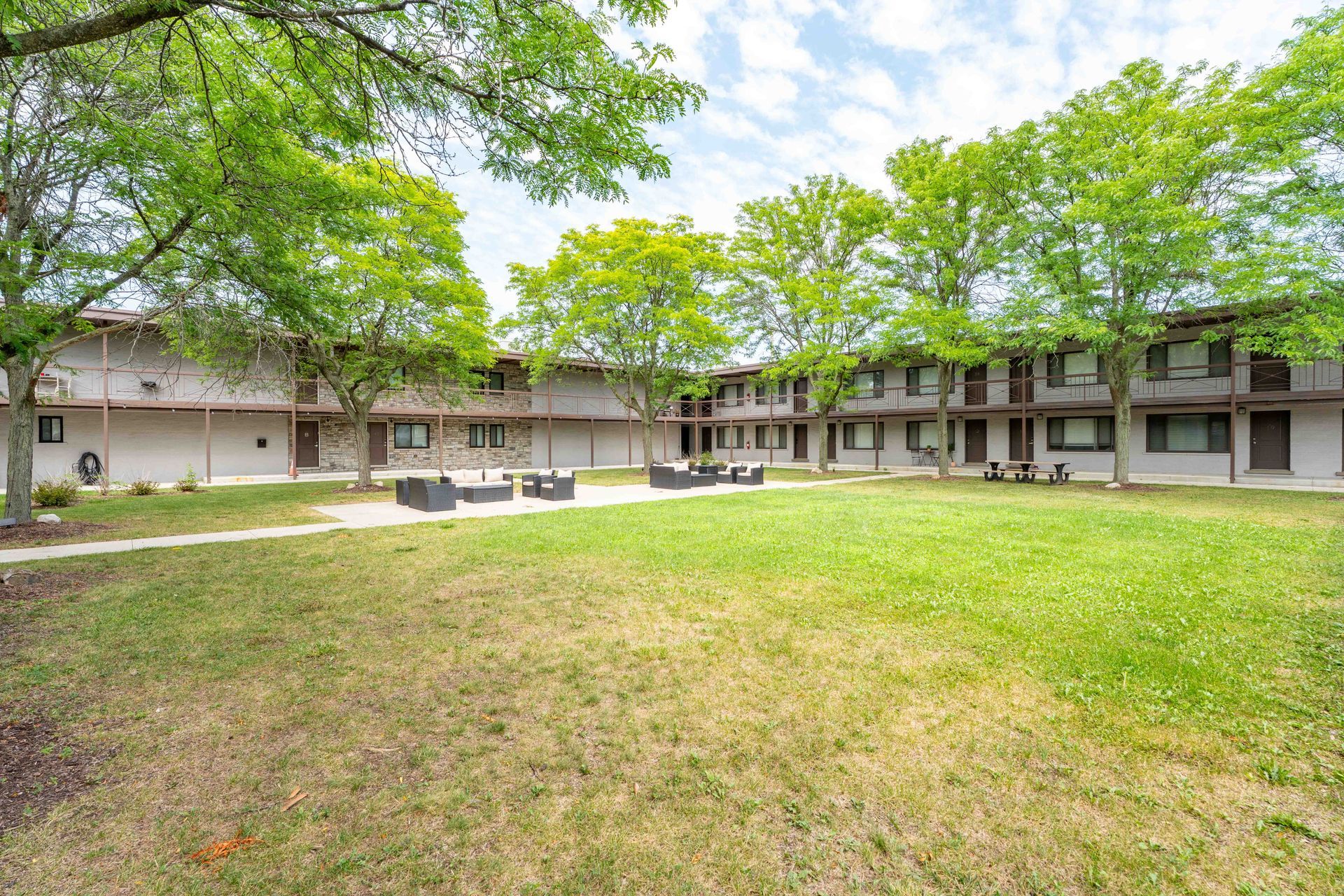 Courtyard with grass, trees, and two-story buildings; seating in the center.