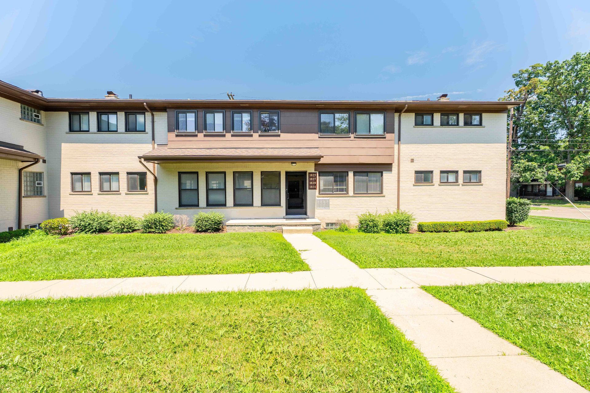 Townhouse exterior with brick and siding, green grass, and a blue sky.