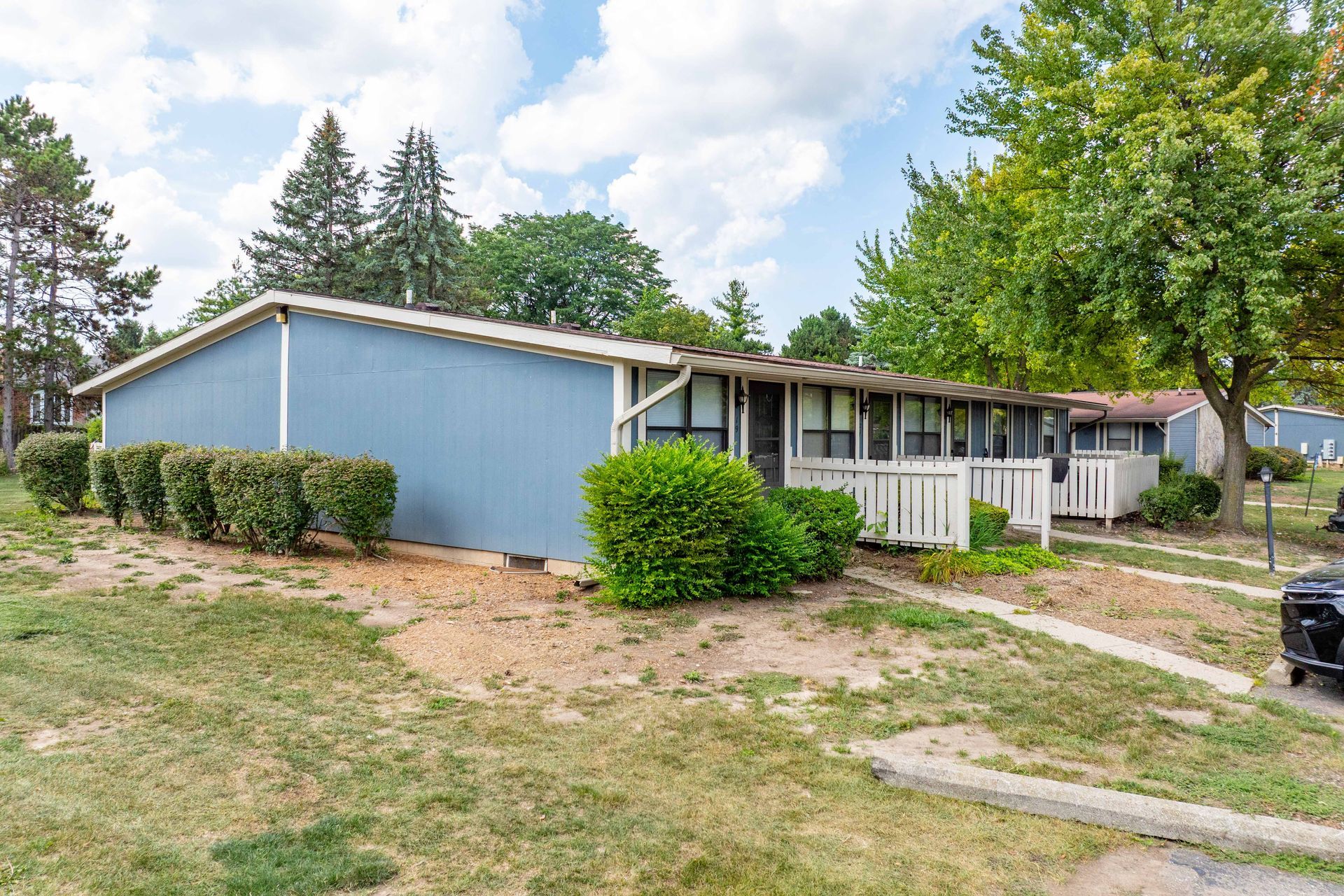 Blue and white townhouses with front porches; green grass and bushes; trees in background.