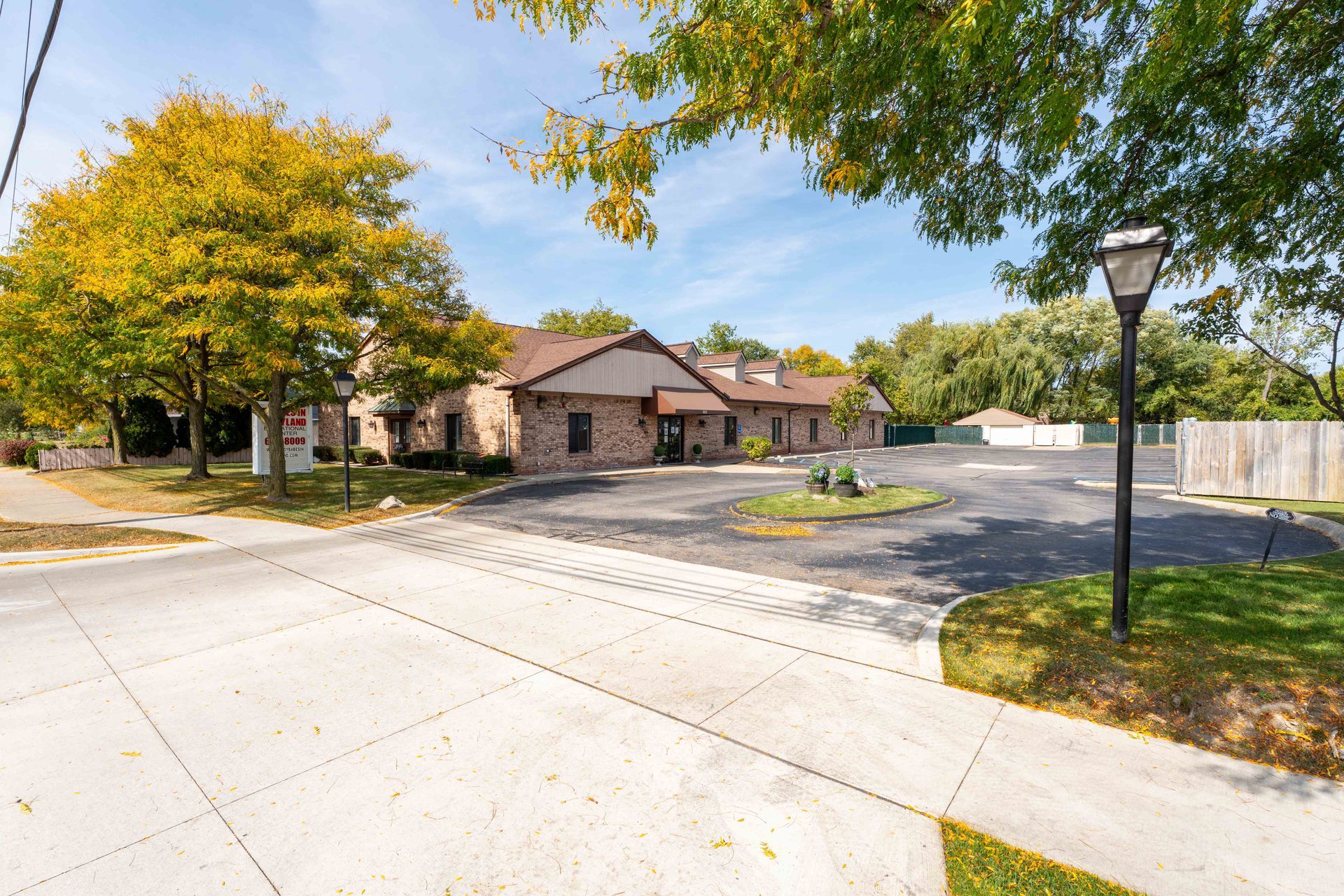 A brick building with a circular driveway, autumn trees, and blue sky.