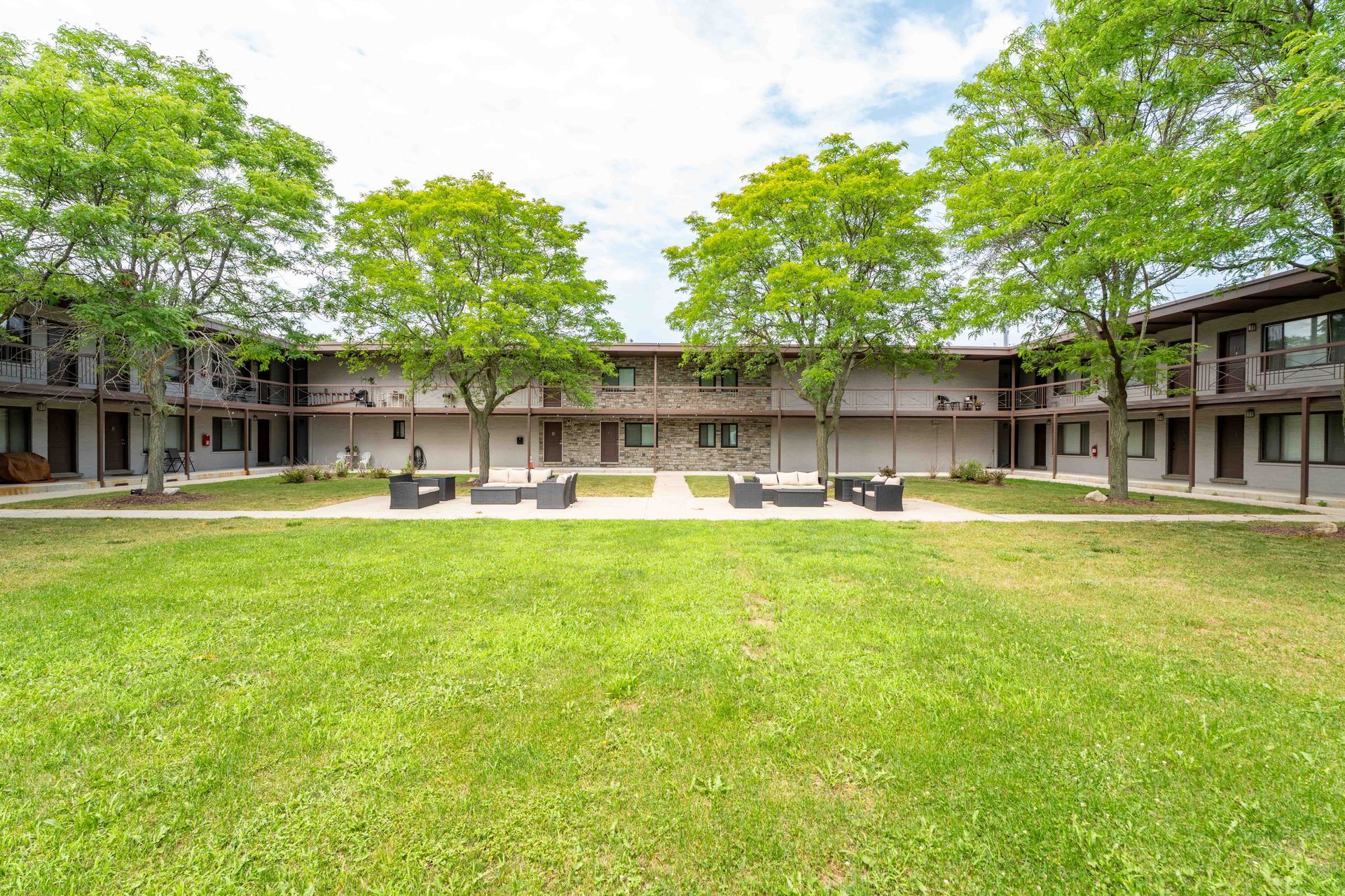 Courtyard apartment complex with a green lawn, trees, and outdoor seating.