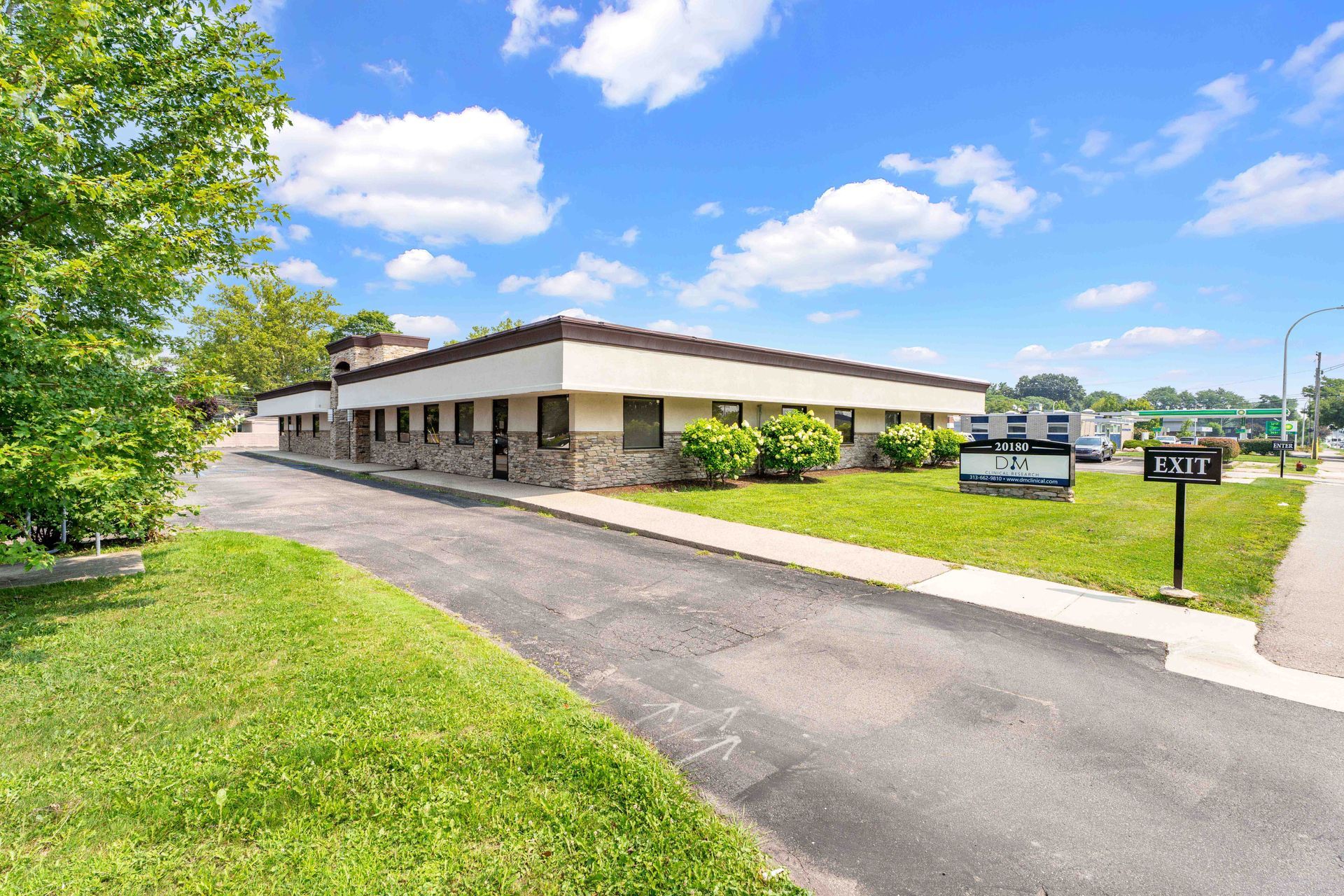 Exterior of a low, one-story commercial building with a stone facade on a sunny day. Green grass and blue sky.