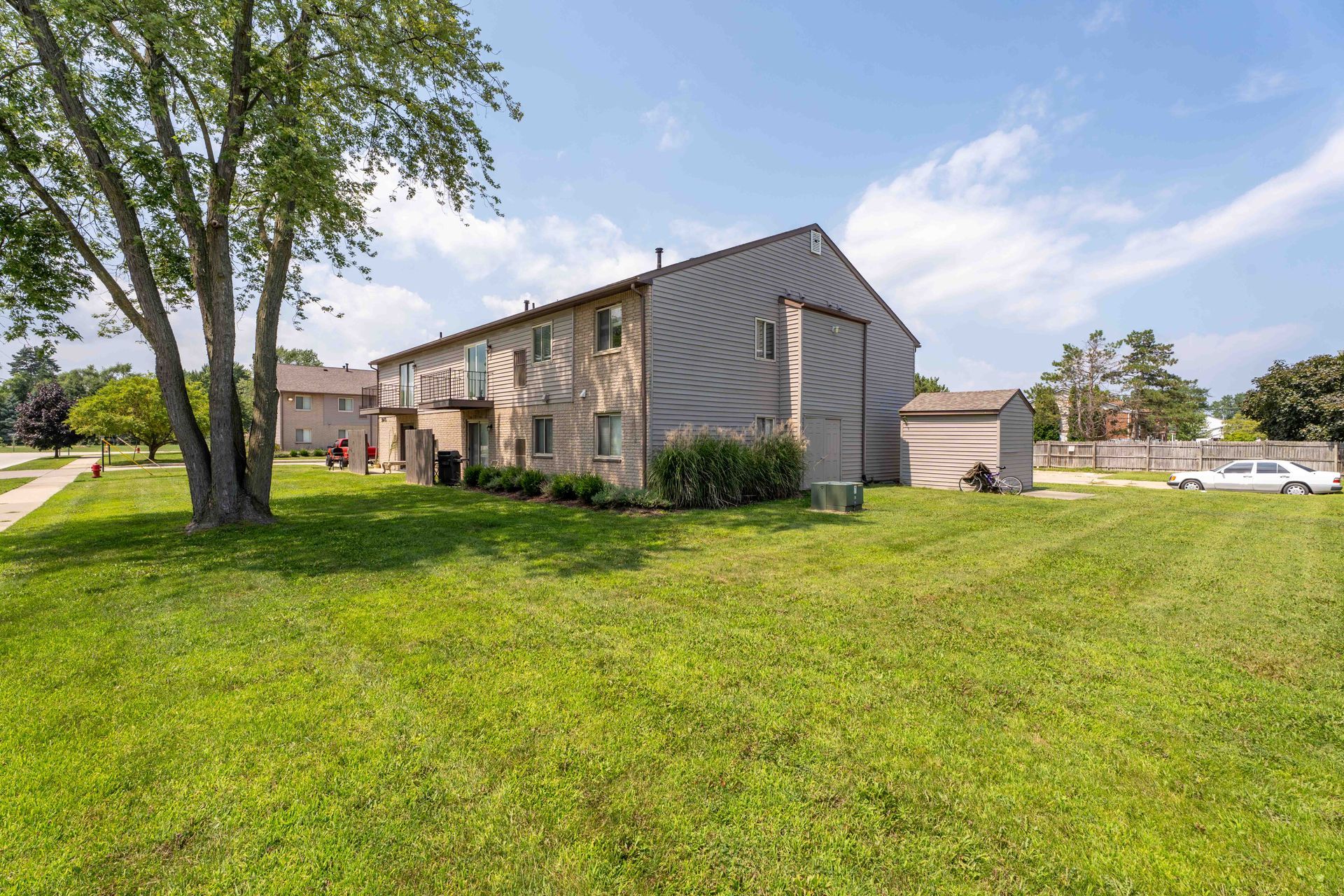 Exterior of a two-story apartment building with a grassy yard on a sunny day.