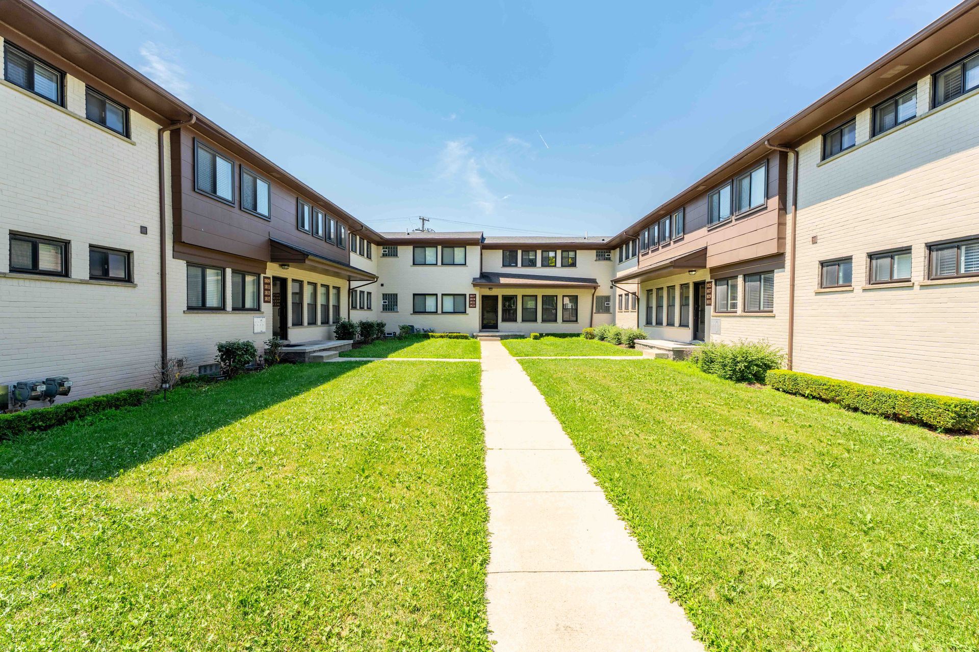 Townhouses with a grassy courtyard and a central walkway under a bright blue sky.