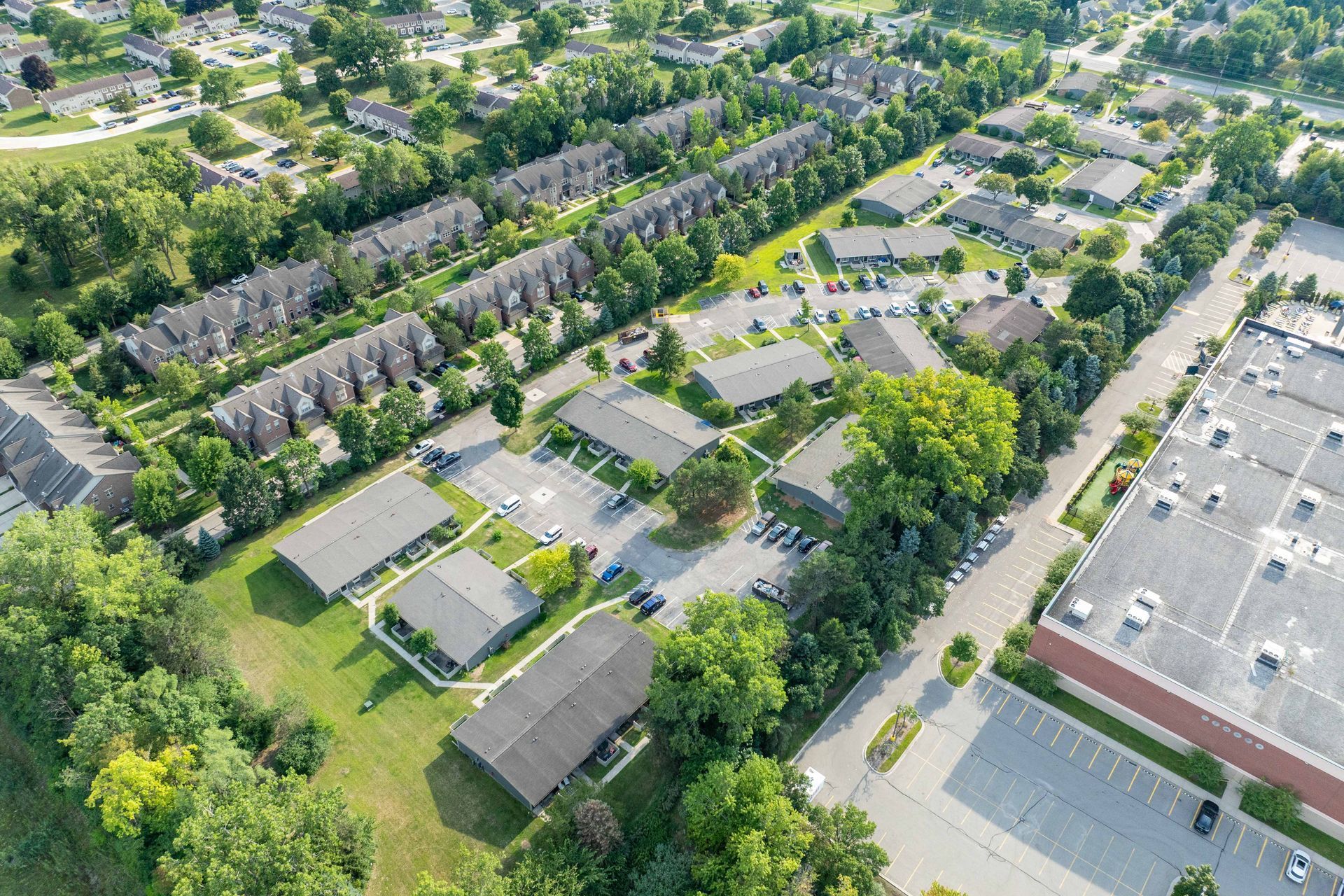 Aerial view of residential buildings surrounded by trees and a parking lot.