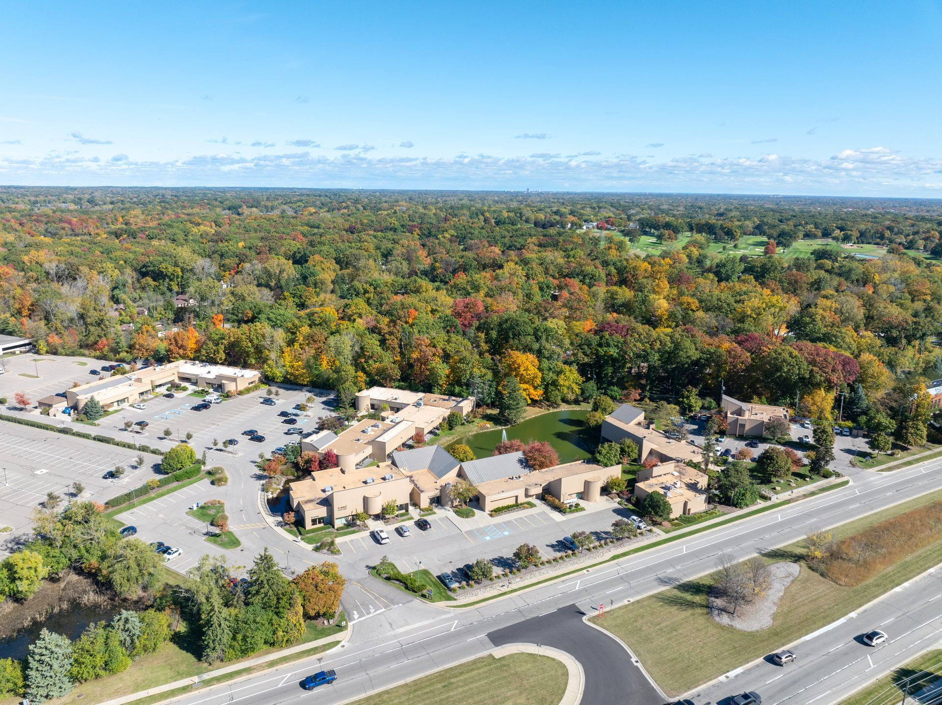 Aerial view of tan buildings, parking lot, and highway surrounded by autumn trees.