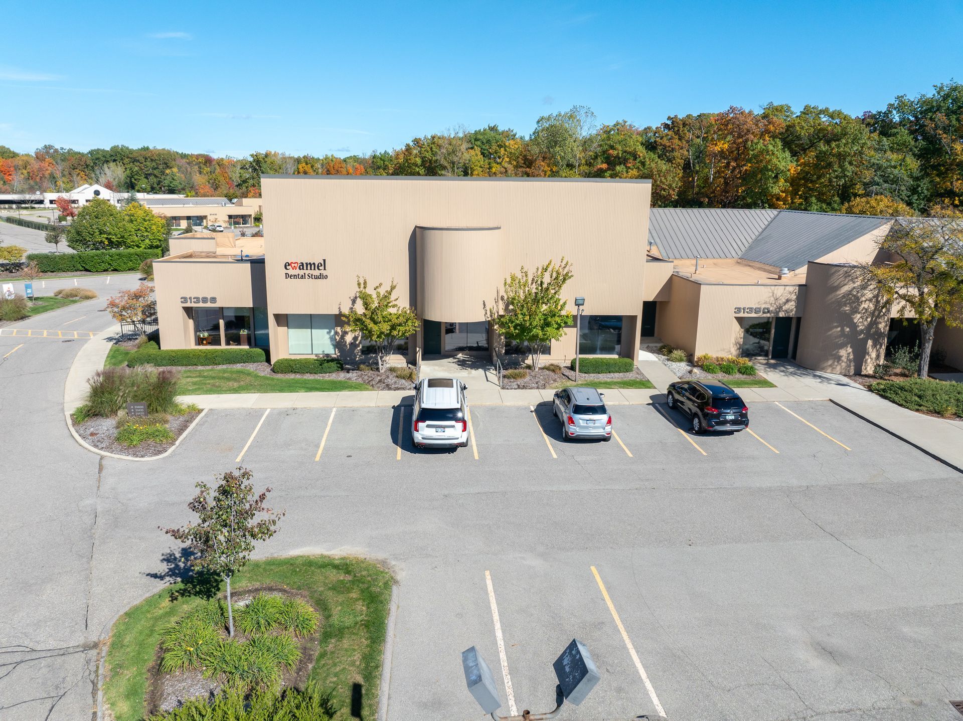 Office building with parked cars, surrounded by parking lot and trees. Sunny day.