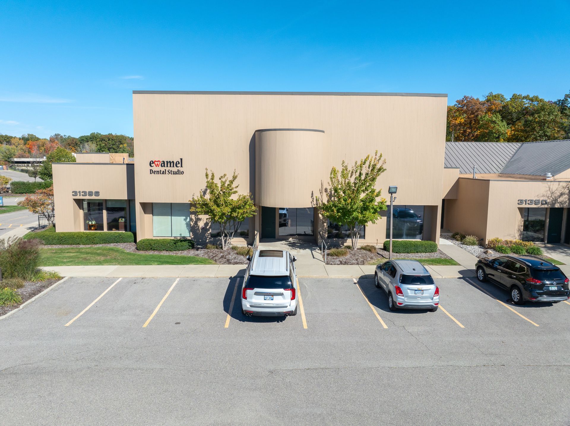 Exterior view of a beige commercial building with a curved entrance, parking lot with cars, and blue sky.
