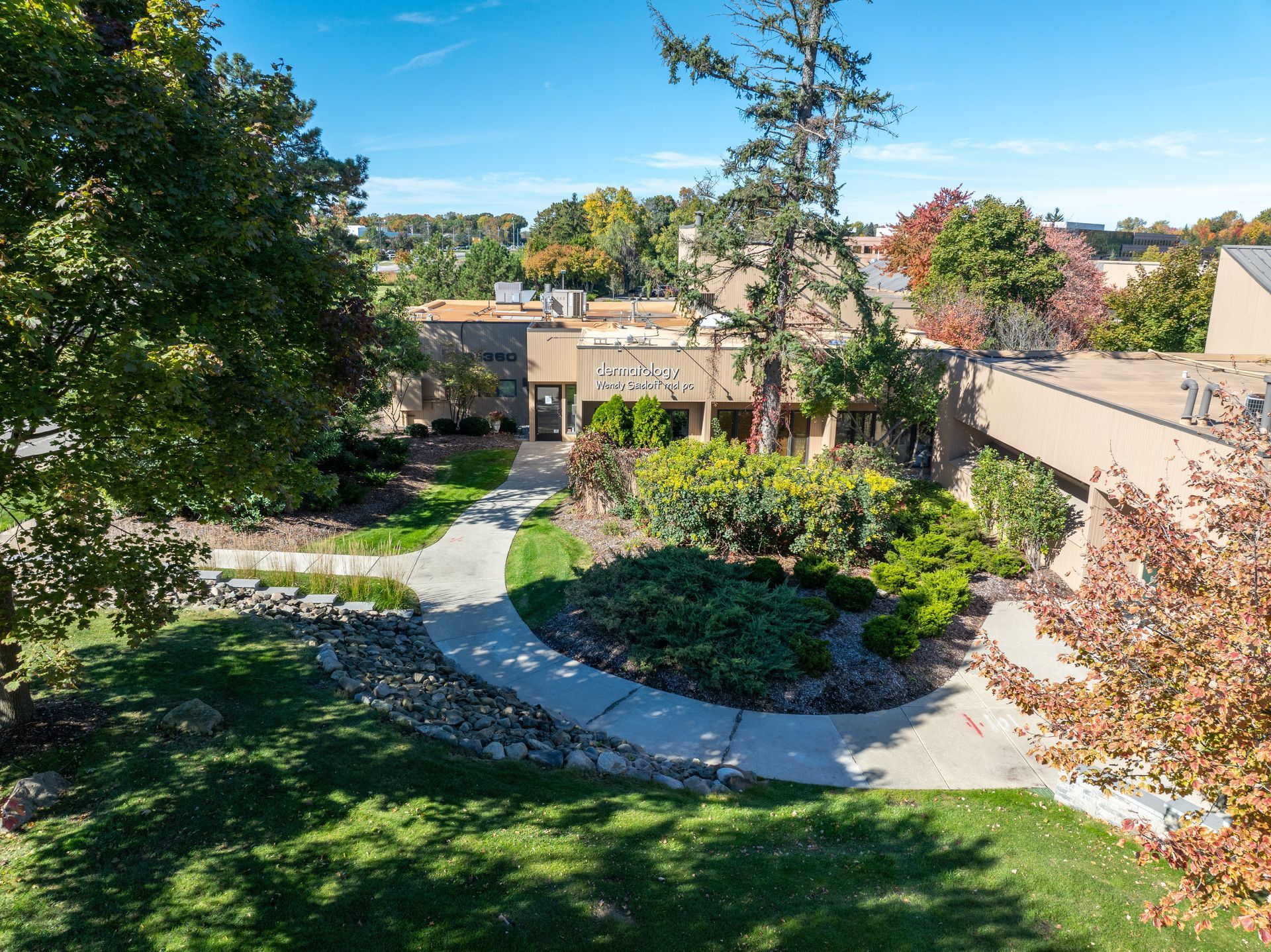 Exterior view of a building with a winding walkway, surrounded by greenery and trees under a blue sky.