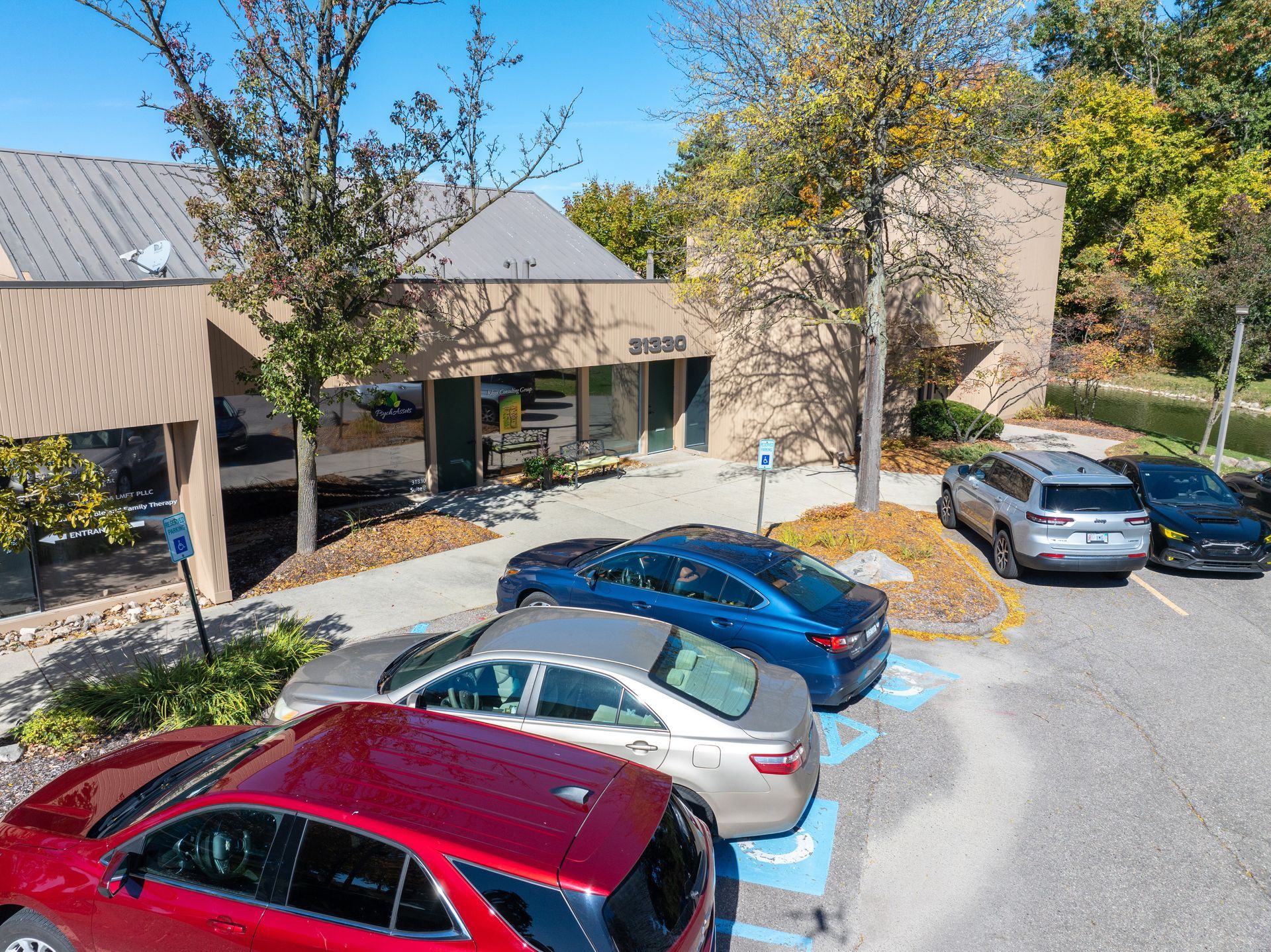 Exterior view of a commercial building with cars parked in front, including a red SUV, blue sedan, and silver sedan.