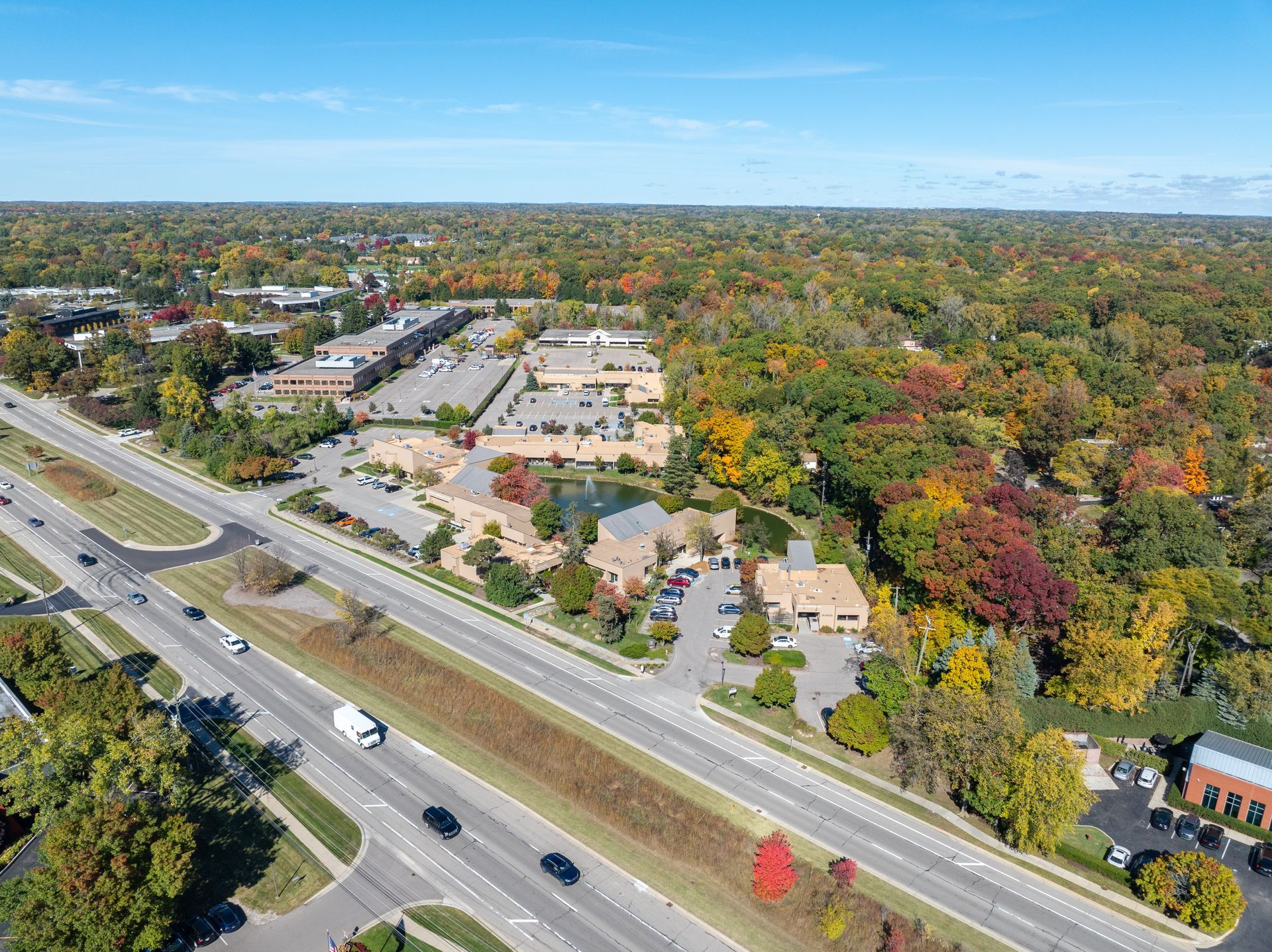 Aerial view of a road with cars, buildings, and colorful trees in autumn.