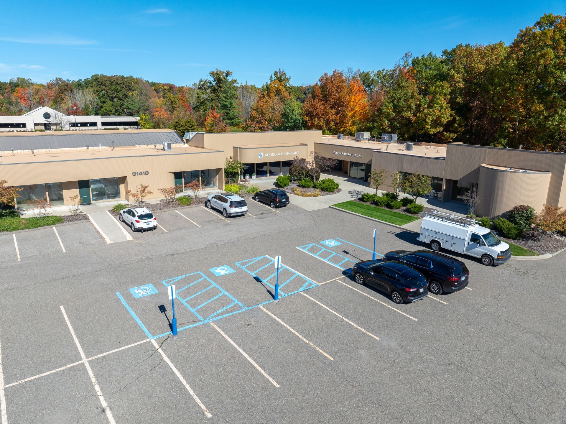 Exterior view of a business complex with parking, accessible spaces, and vehicles on a sunny day.