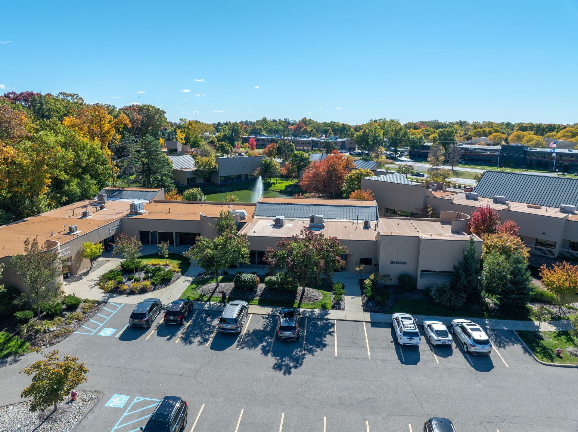 Aerial view of a beige building with cars parked in front and trees surrounding it under a blue sky.