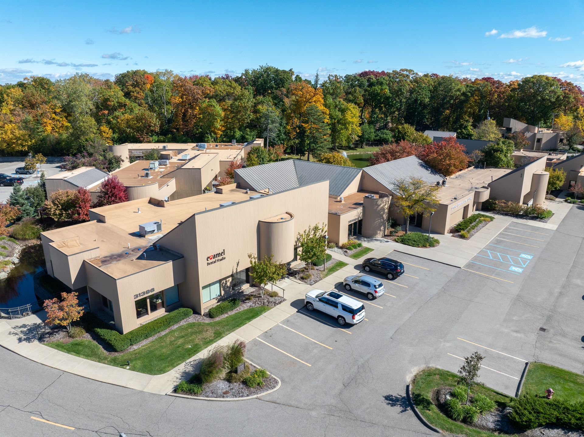 An aerial view of a tan building with cars parked out front, surrounded by trees.