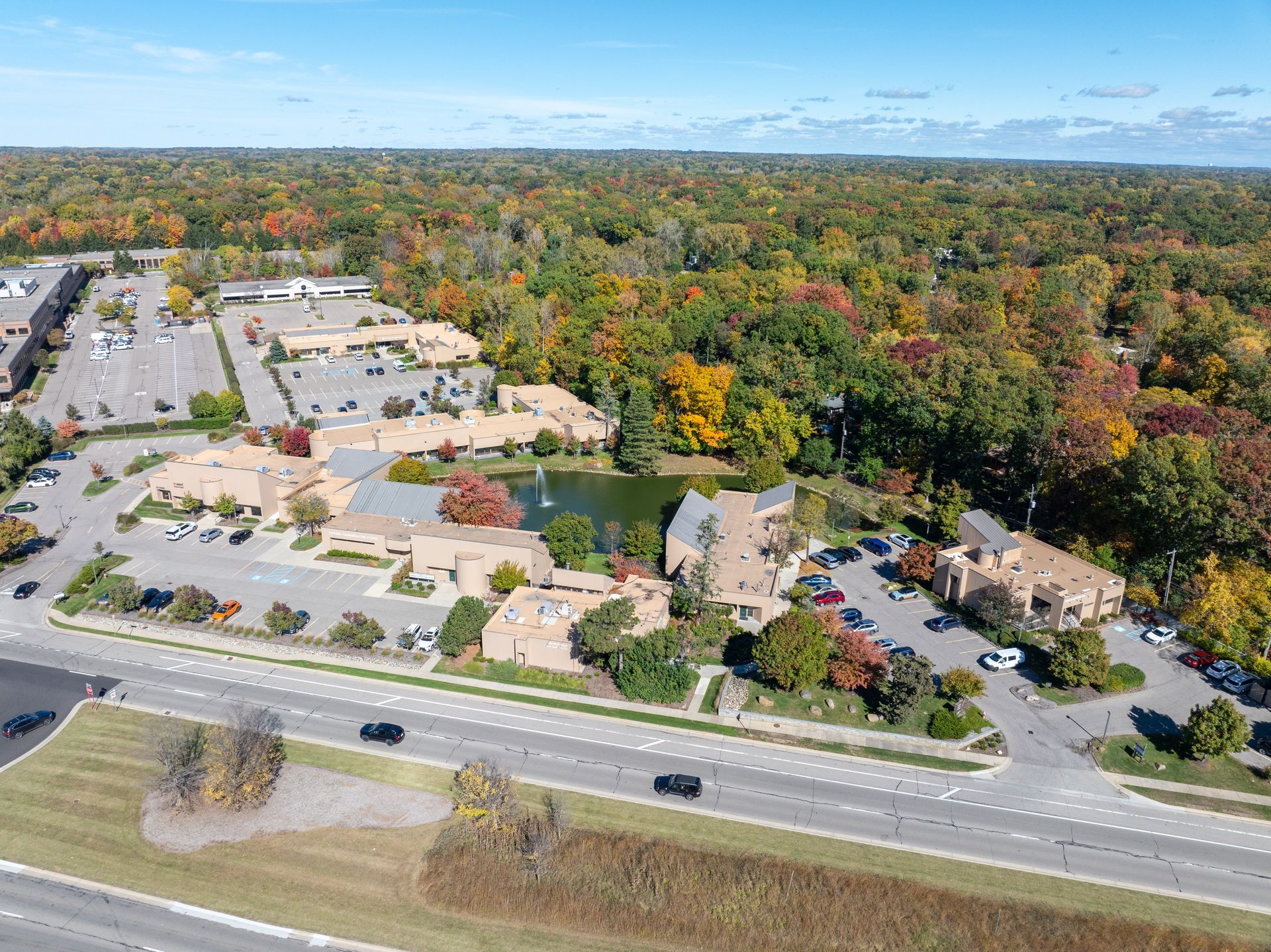 Aerial view of buildings with a lake, surrounded by a forest of colorful autumn trees.