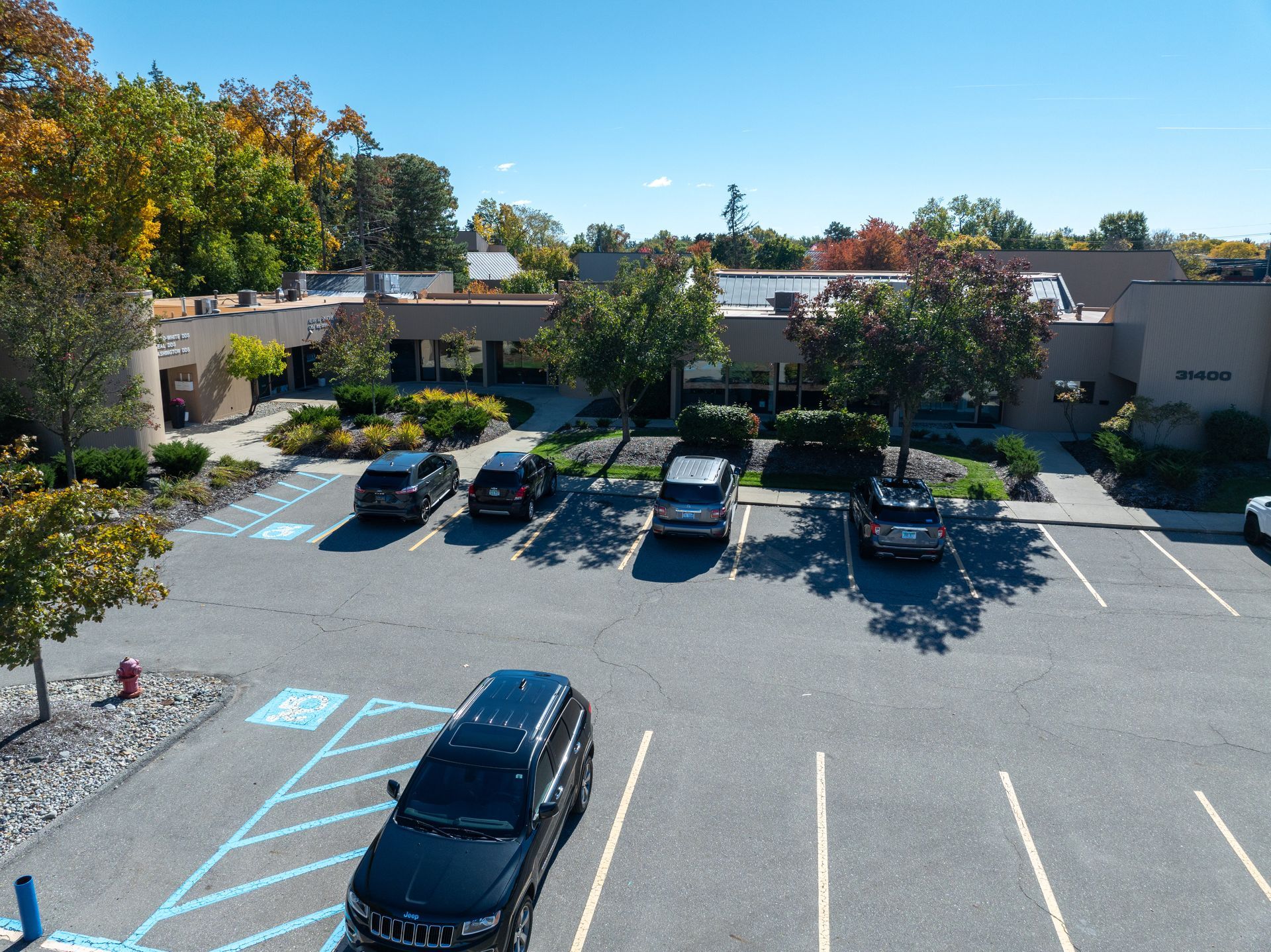 Aerial view of a building with a parking lot. Cars parked outside a low, brown building on a sunny day.