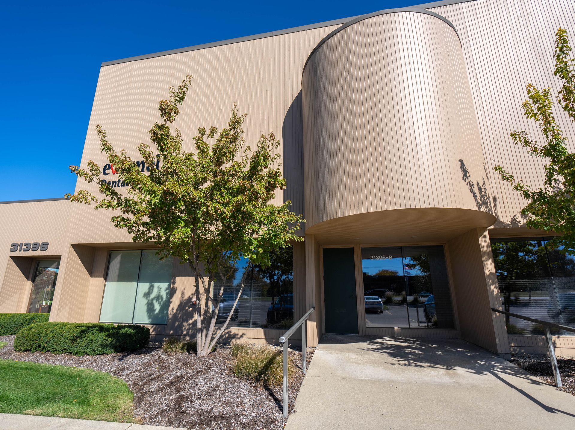 Beige office building with a curved facade and entryway, blue sky.
