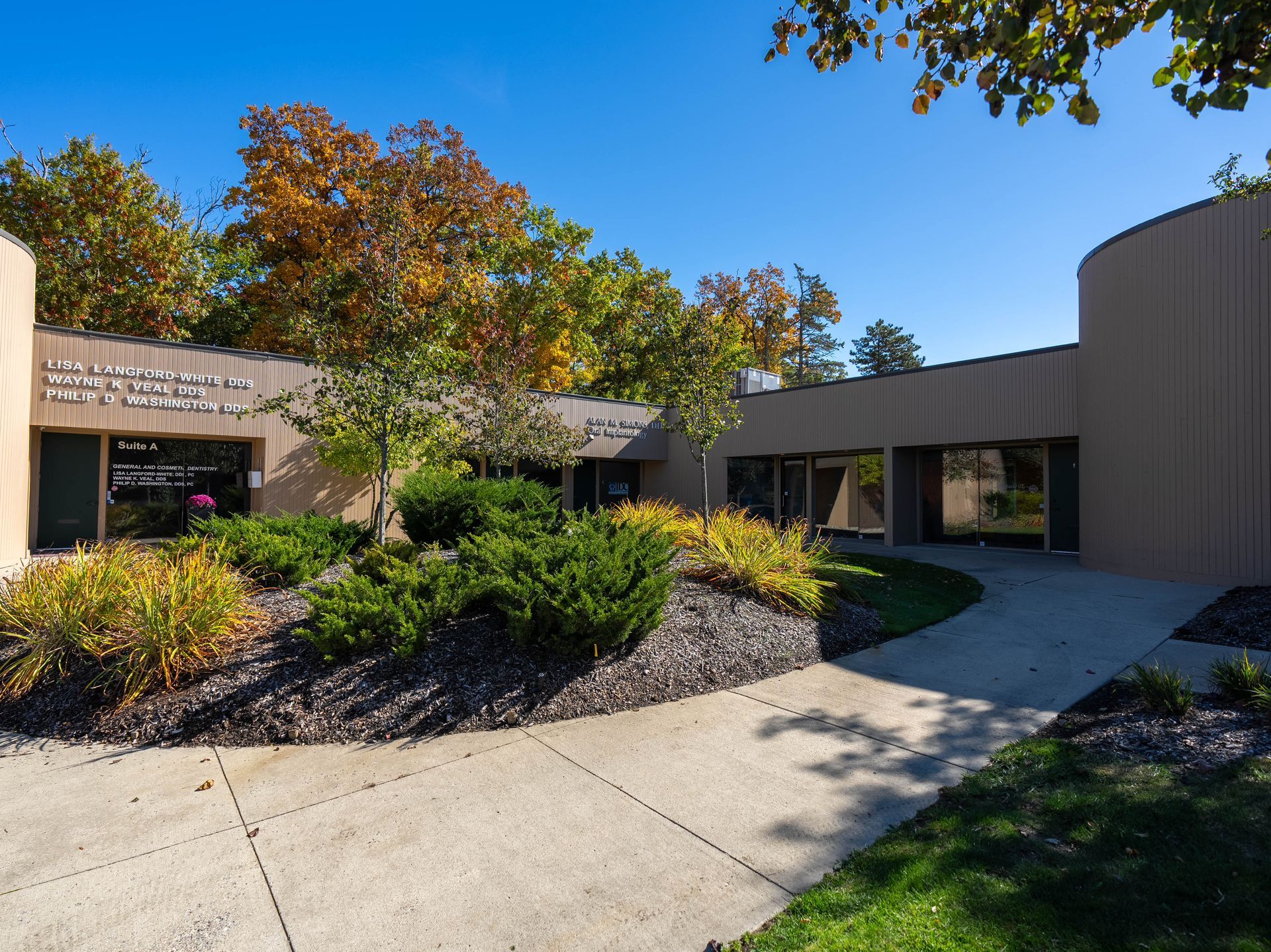 Exterior of a tan building with a curving facade, landscaping, and a walkway on a sunny day.