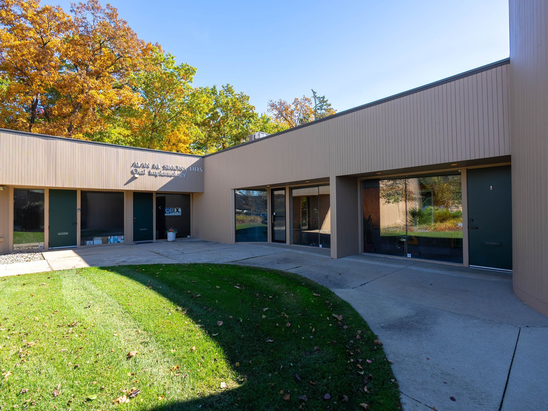 Tan building with glass doors and windows, grassy courtyard, trees with fall foliage.