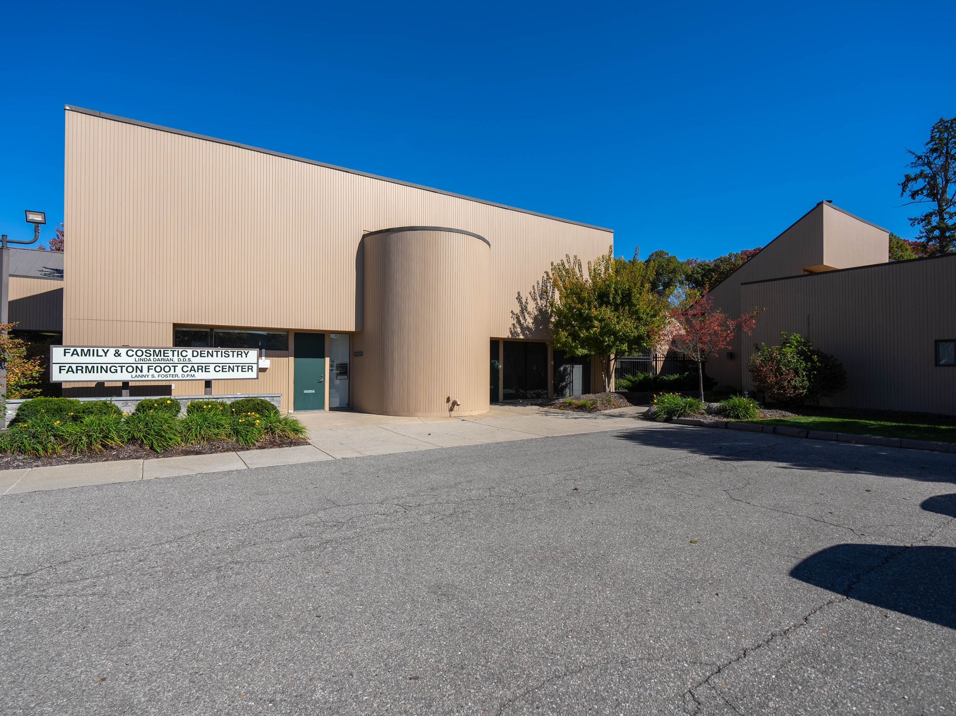 Tan building with sign; entrance with curved wall, gravel parking area, blue sky.