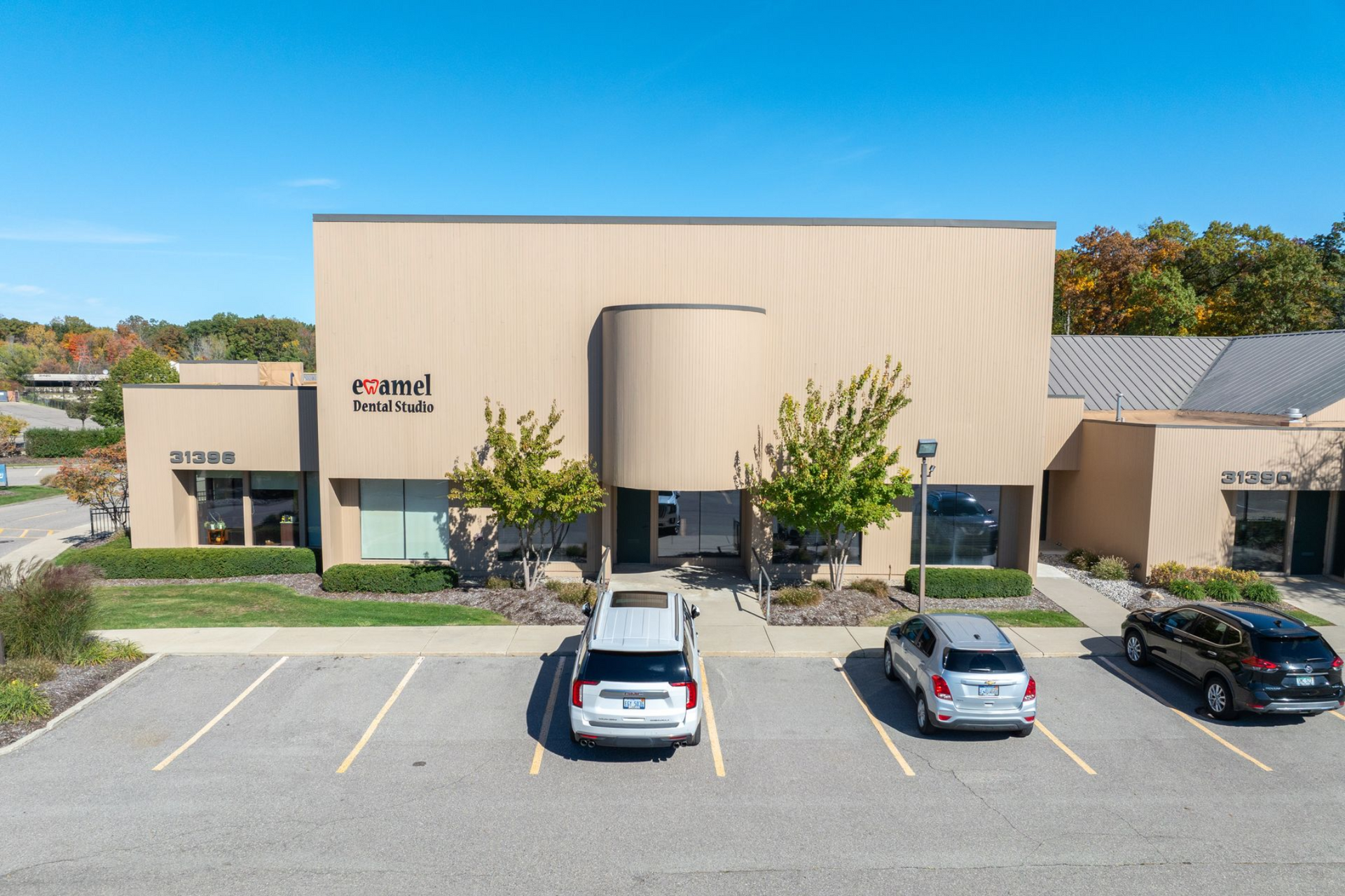 Exterior of a beige office building with a curved entry, cars parked in front, clear blue sky.