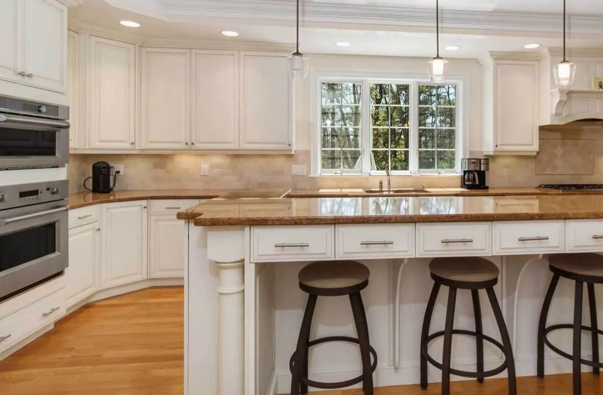 Kitchen with white cabinets, brown countertop, and three brown bar stools